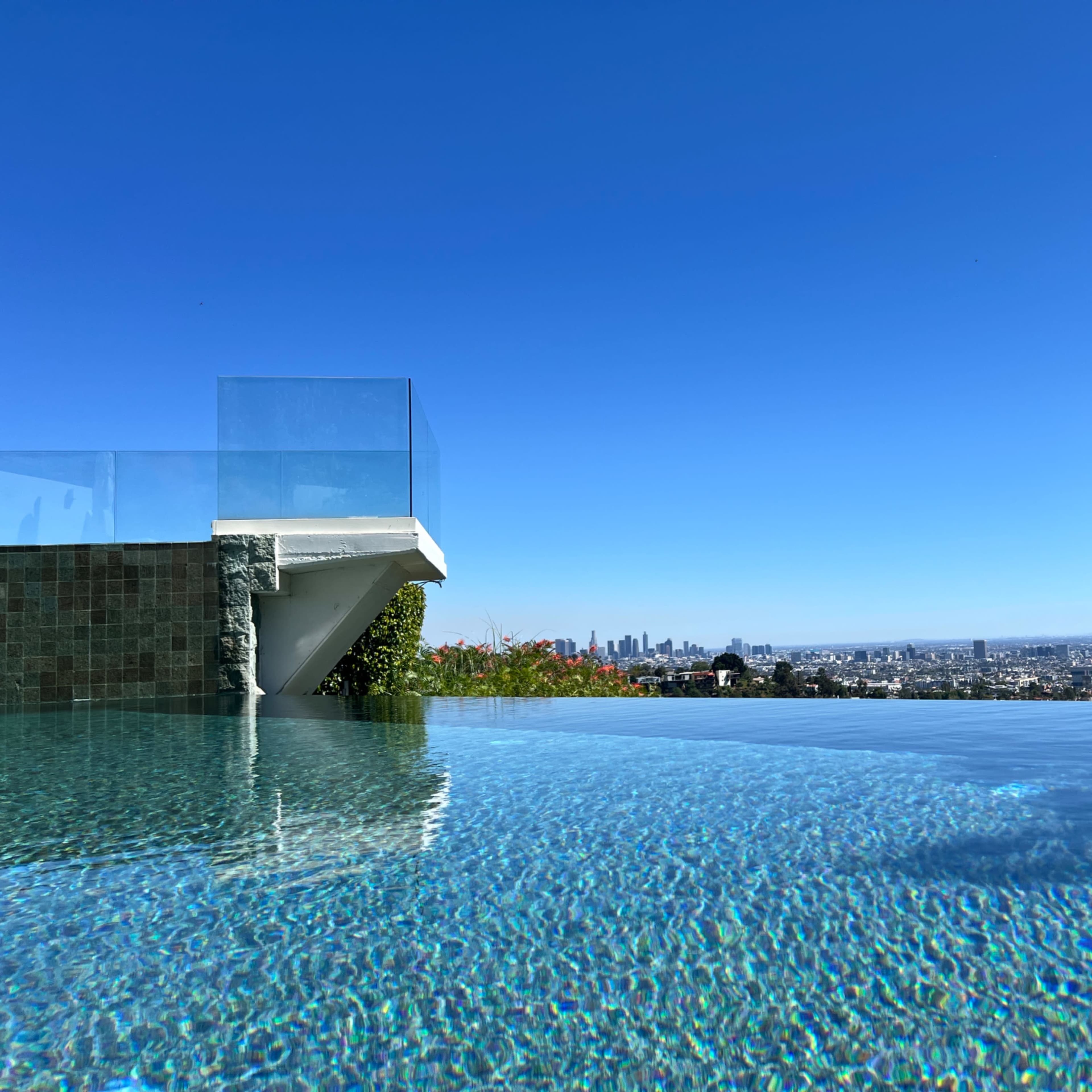A luxurious infinity pool reflects the clear blue sky and offers a panoramic view of the city skyline.