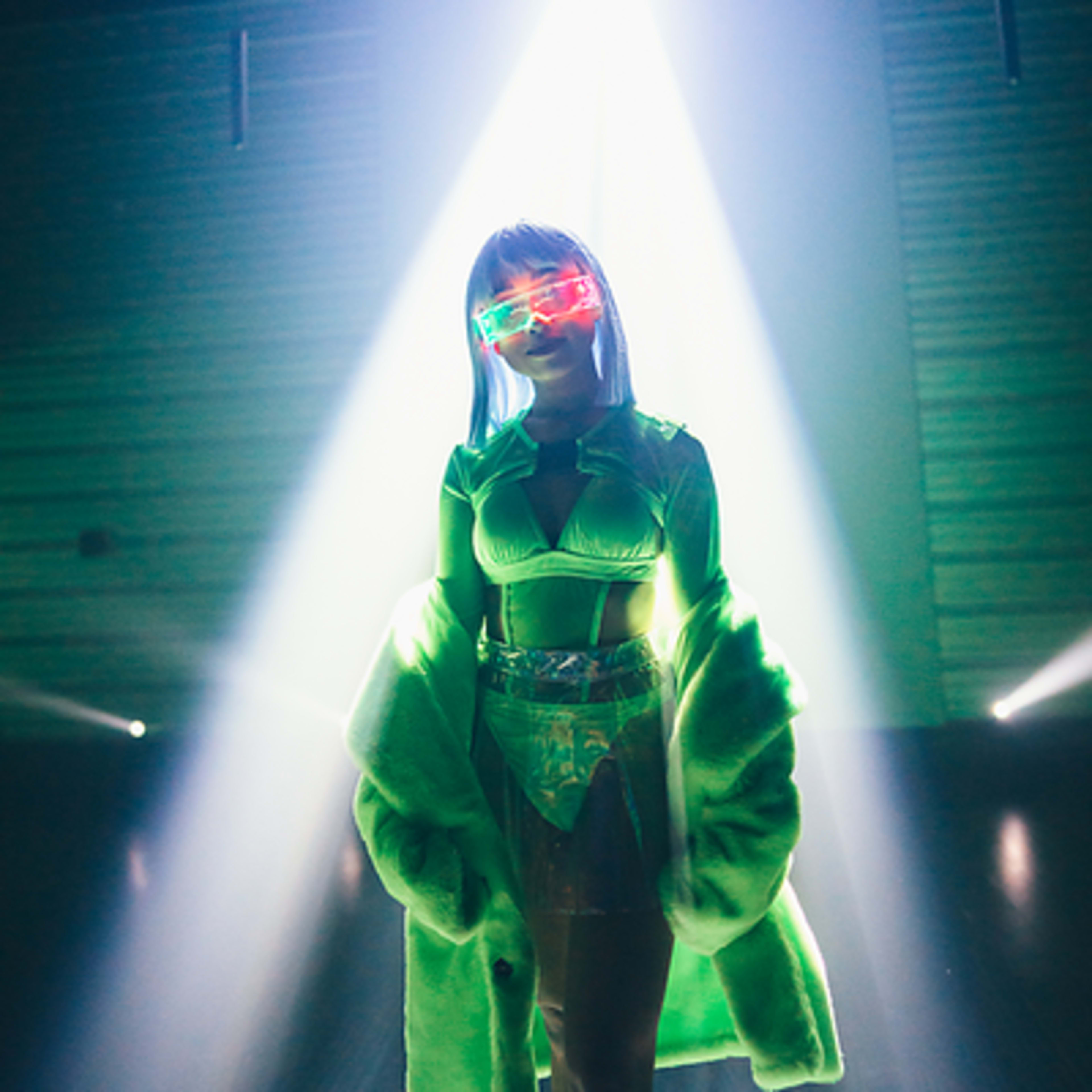 A person dressed in a brightly colored outfit stands illuminated by a beam of light on a stage.