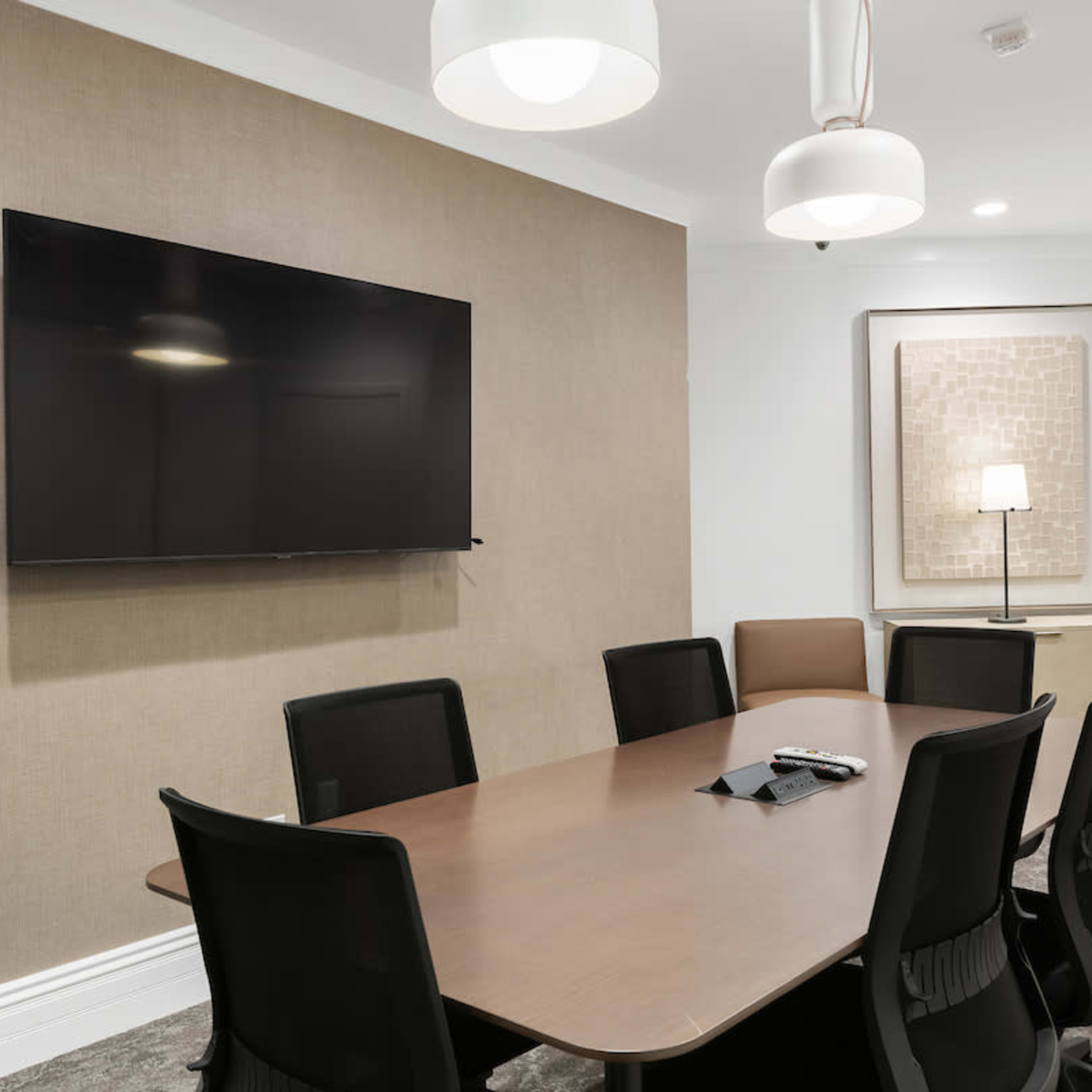 A modern meeting room with a large table, eight black chairs, a wall-mounted television, and a decorative piece on the wall.