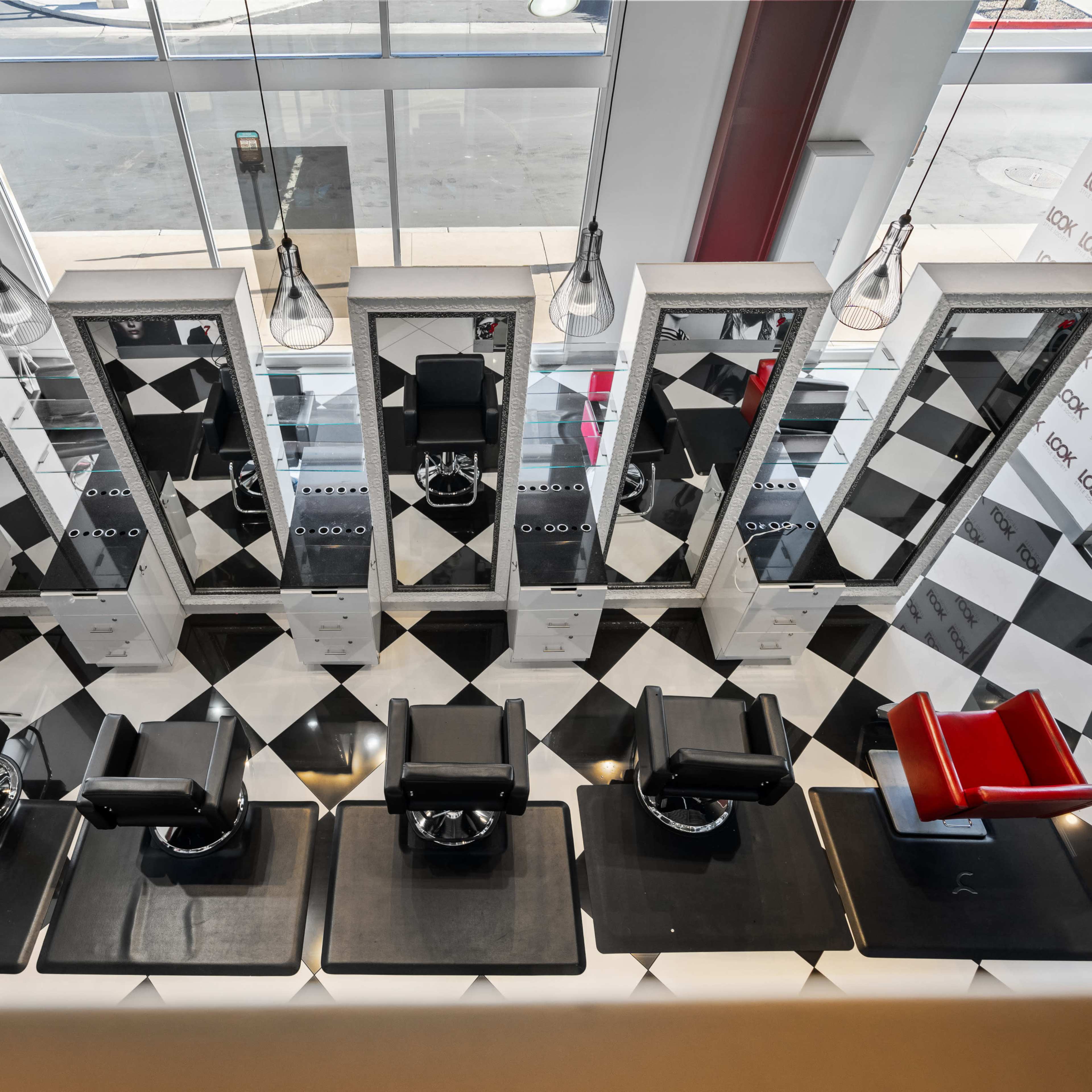 An aerial view of a barber shop with six black barber chairs arranged in front of mirrors on a checkered floor.