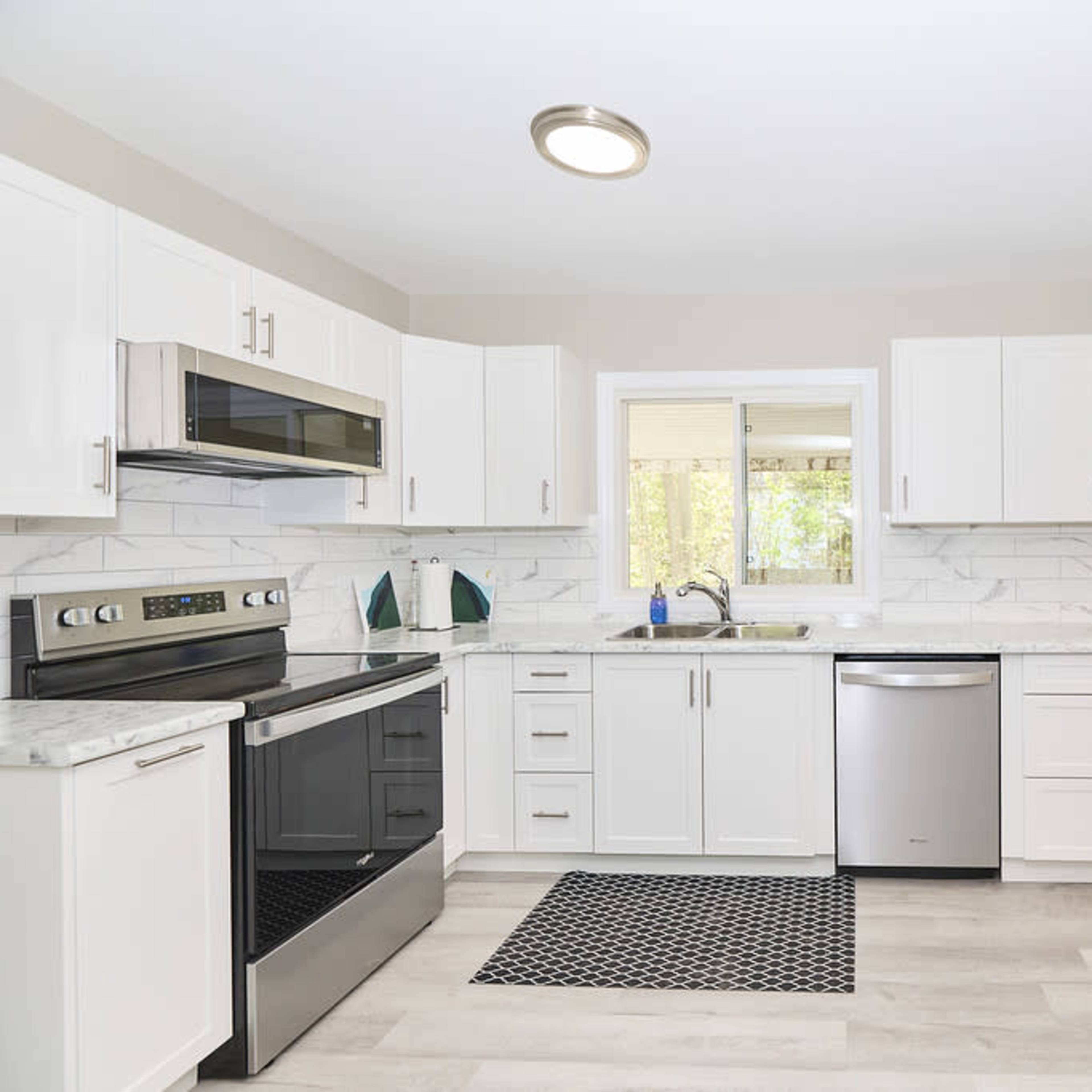 A modern kitchen features stainless steel appliances, white cabinetry, and a marble countertop with a window above the sink.