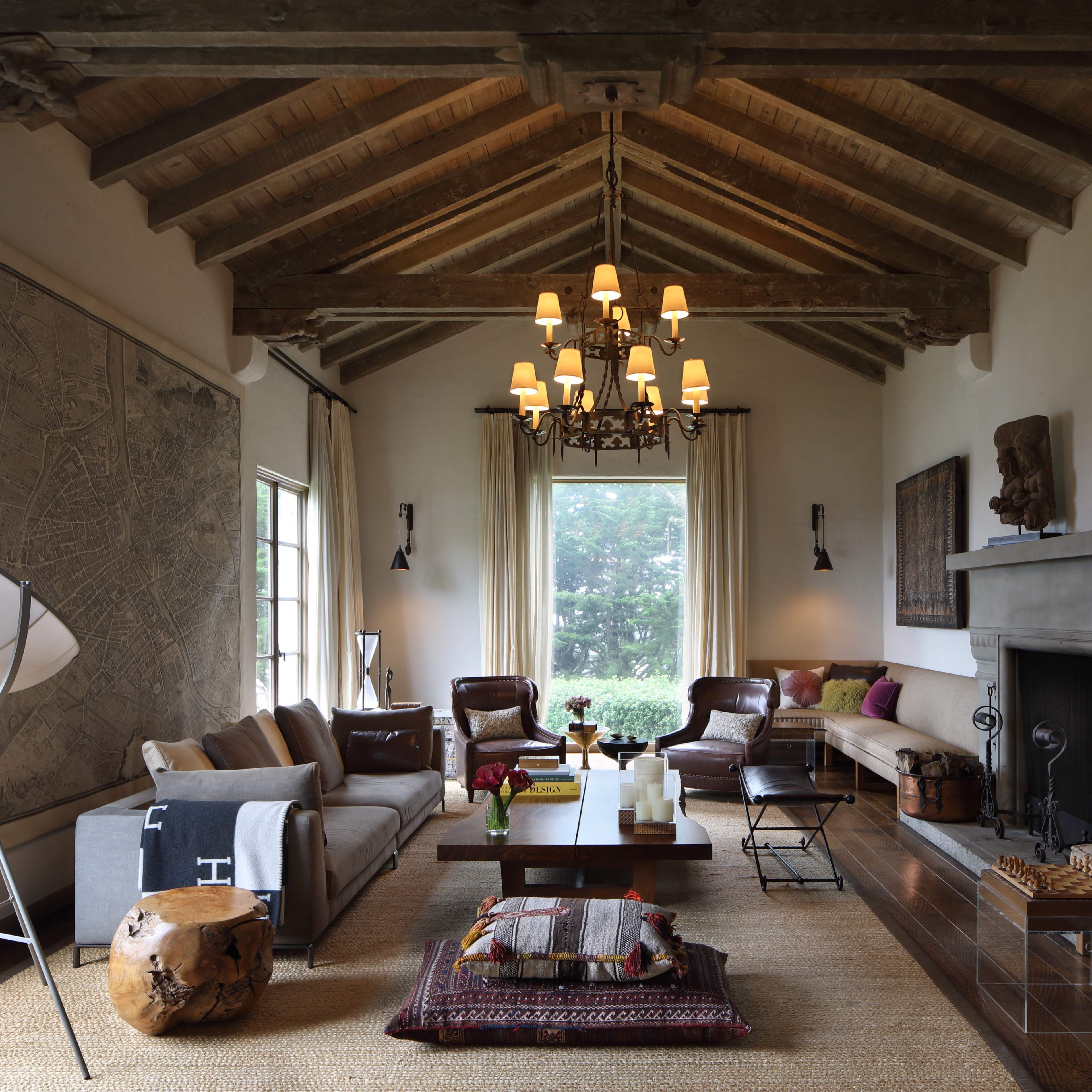 The living room features a high-beamed ceiling, a fireplace, and a mix of modern and rustic furnishings arranged around a central coffee table.