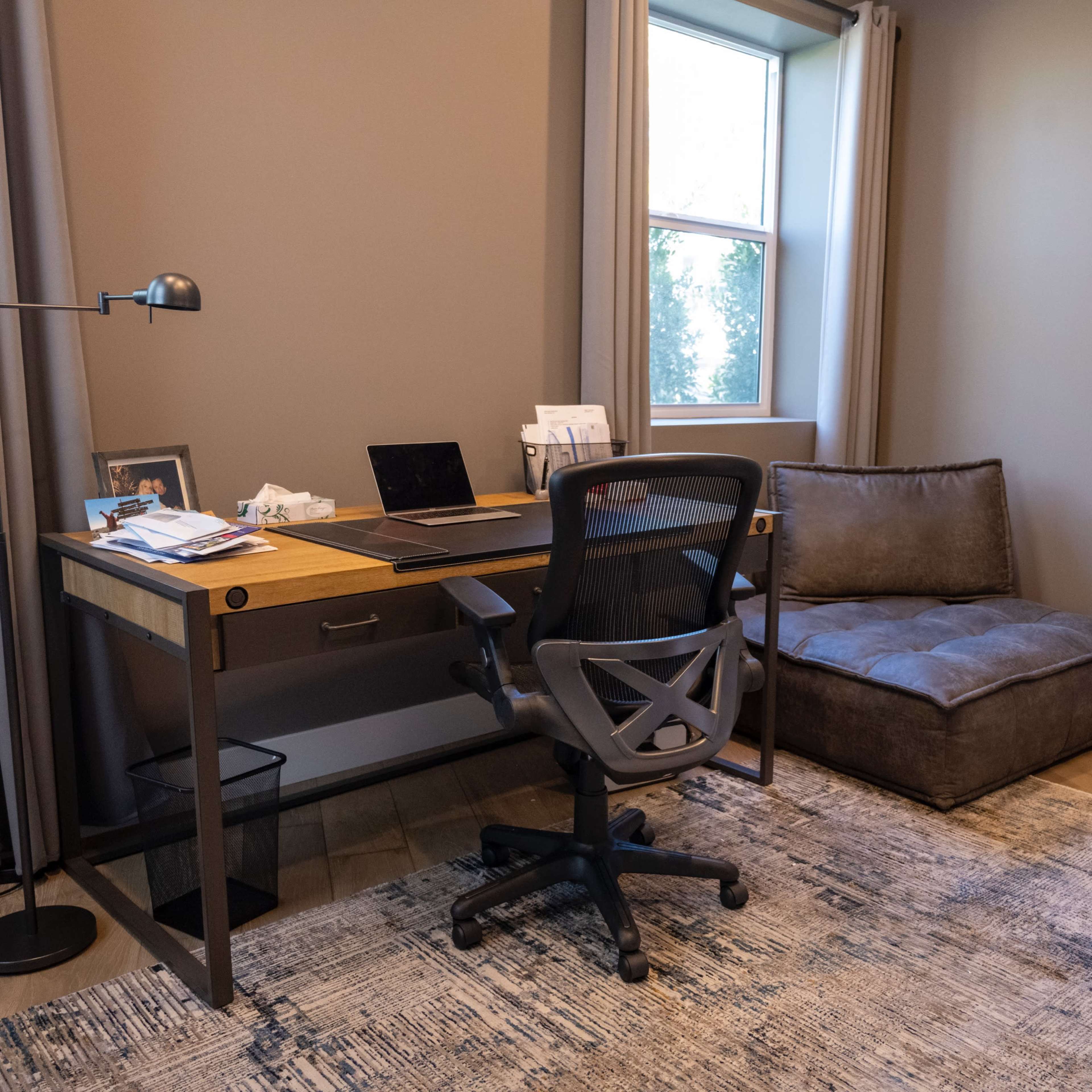 A modern home office with a desk, chair, and a seating area beside a window.