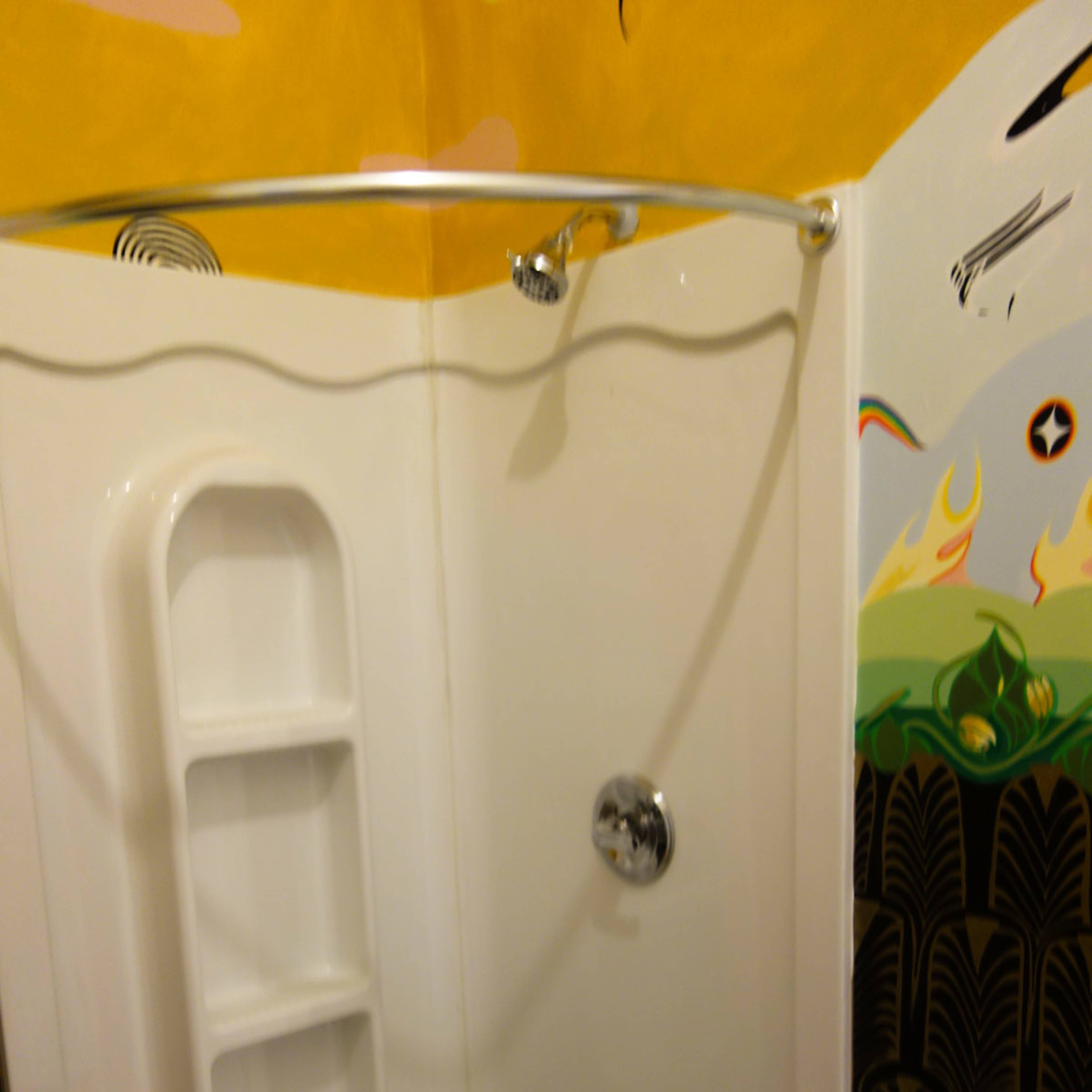 A white corner shower stall with built-in shelving, a showerhead, and a chrome faucet set against a colorful wall mural.