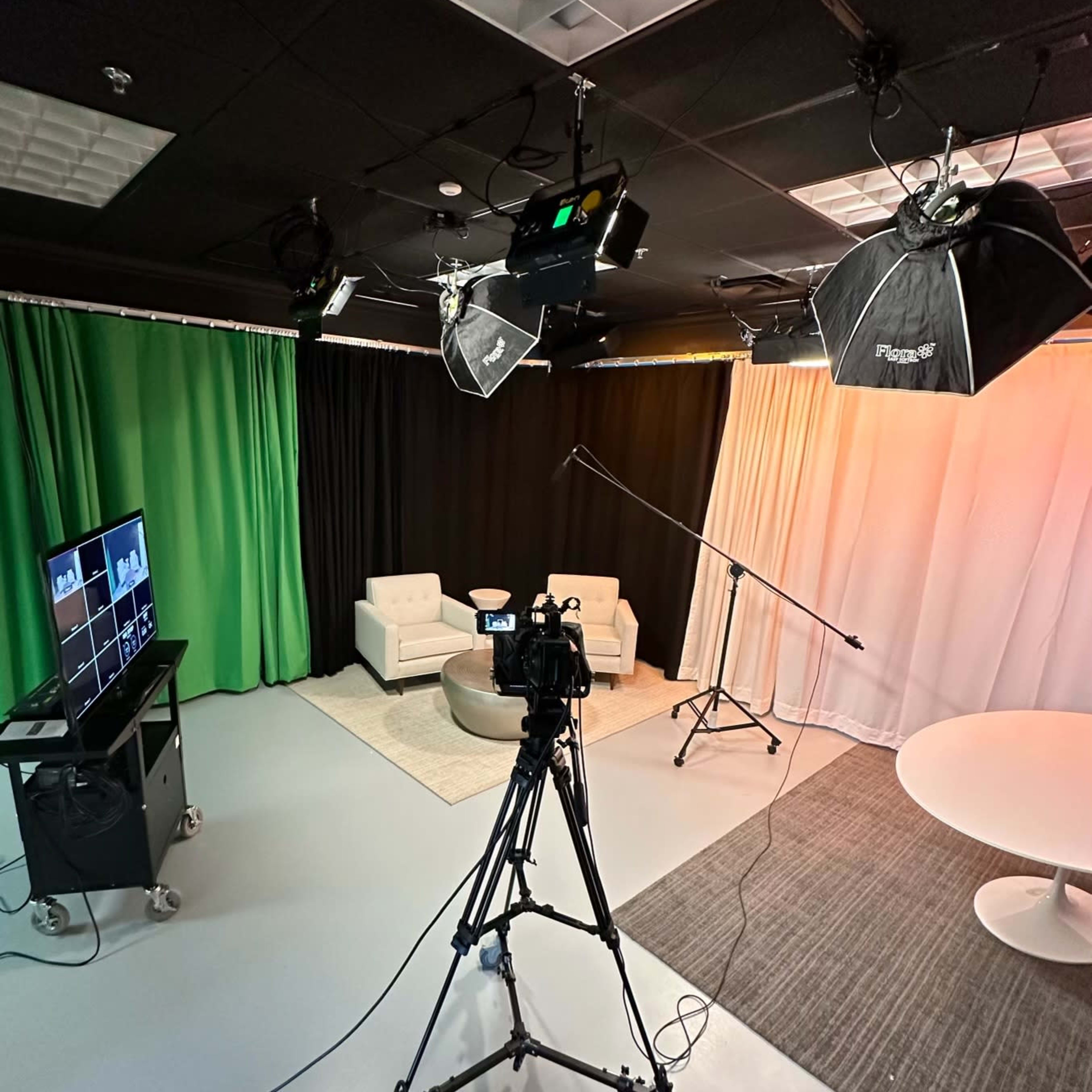 A video production studio with a camera on a tripod, lighting equipment, and various backdrops, including green and black curtains.