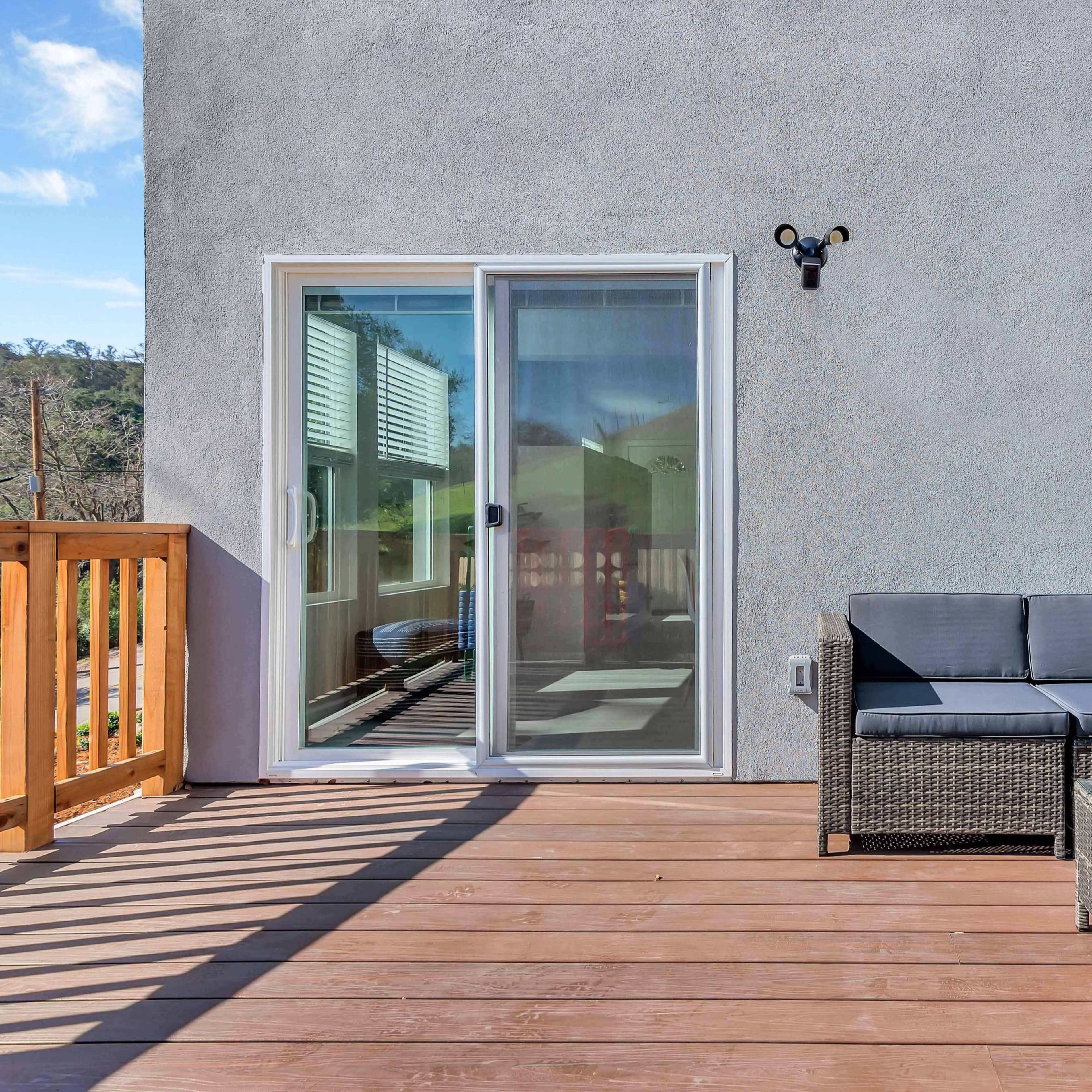 A patio features a seating area with a gray wicker sofa and glass-top coffee table, adjacent to sliding glass doors.