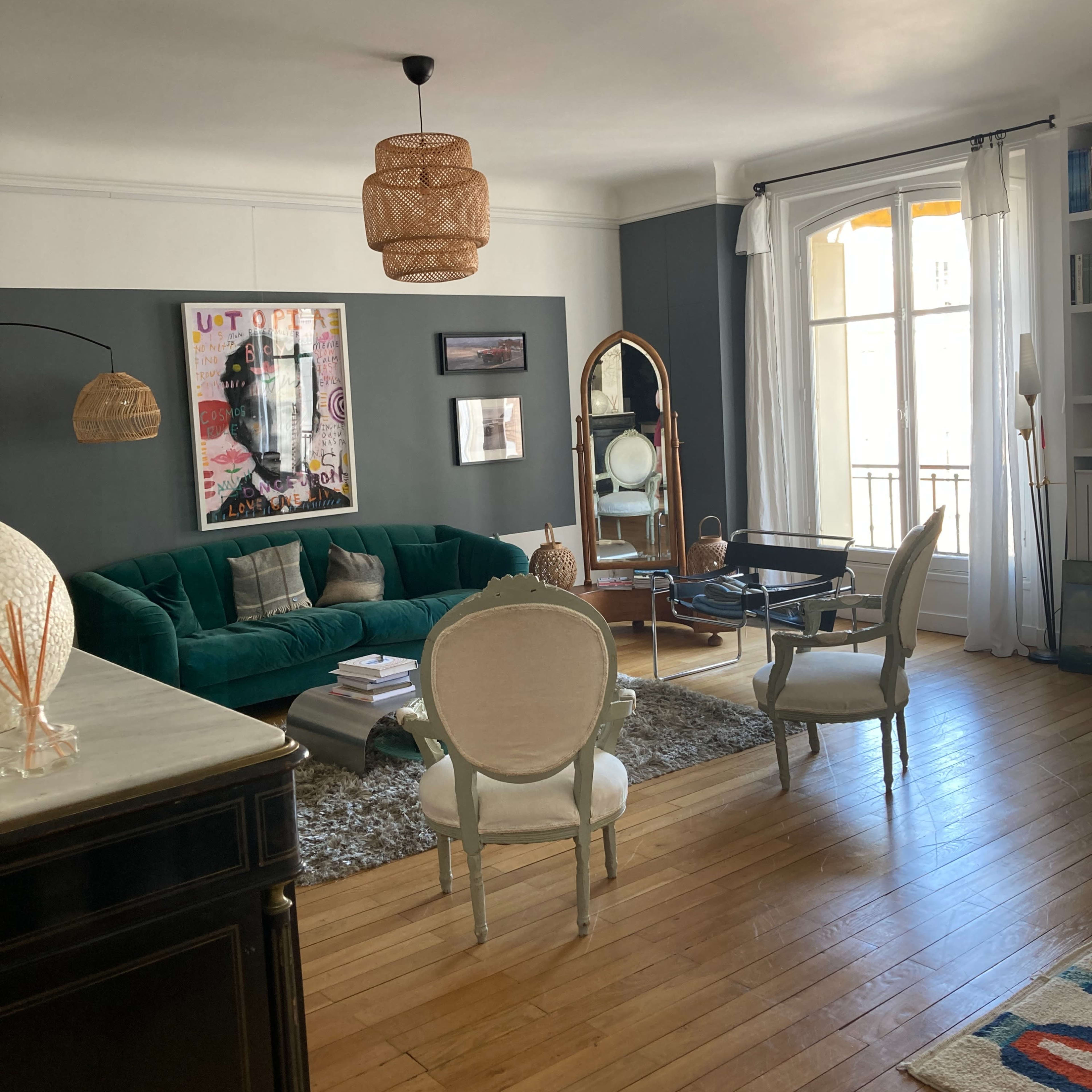 A living room featuring a green sofa, a wooden floor, and various decorative elements, including a mirror and wall art.