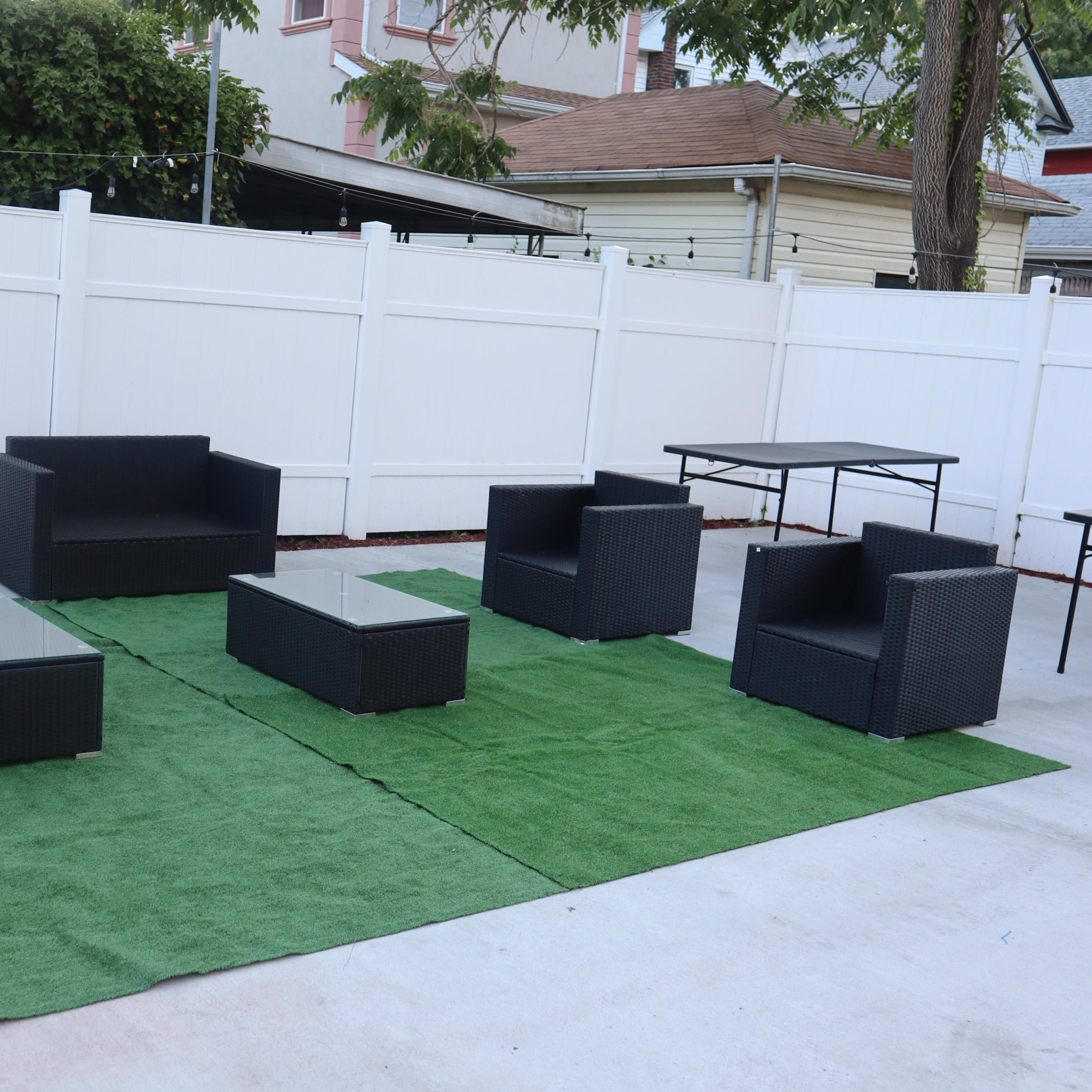 A patio area features a set of black wicker furniture, including a sofa, chairs, and a glass-topped coffee table, arranged on green artificial grass.