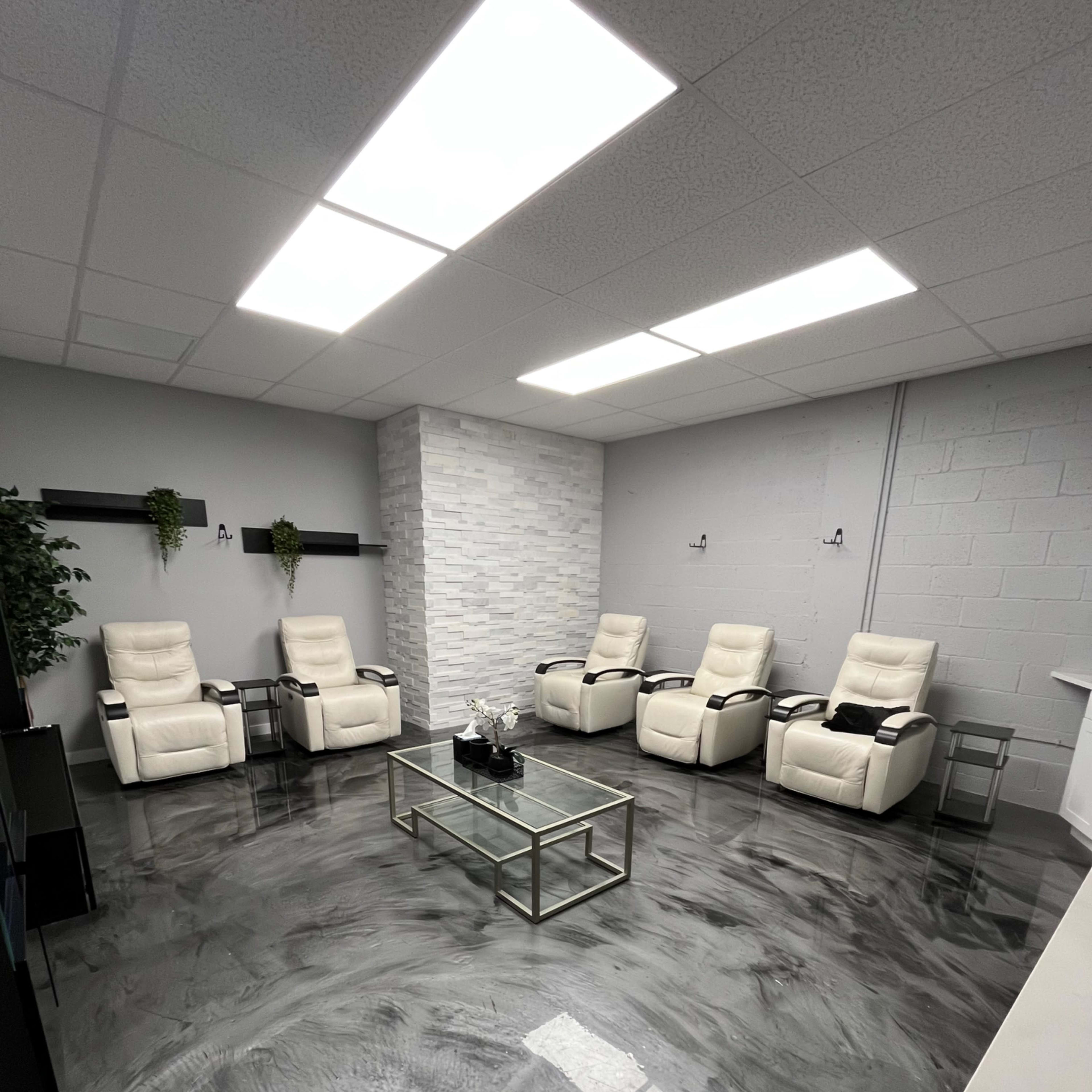 A modern room with four reclining chairs arranged around a glass coffee table, featuring a polished concrete floor and a stone accent wall.