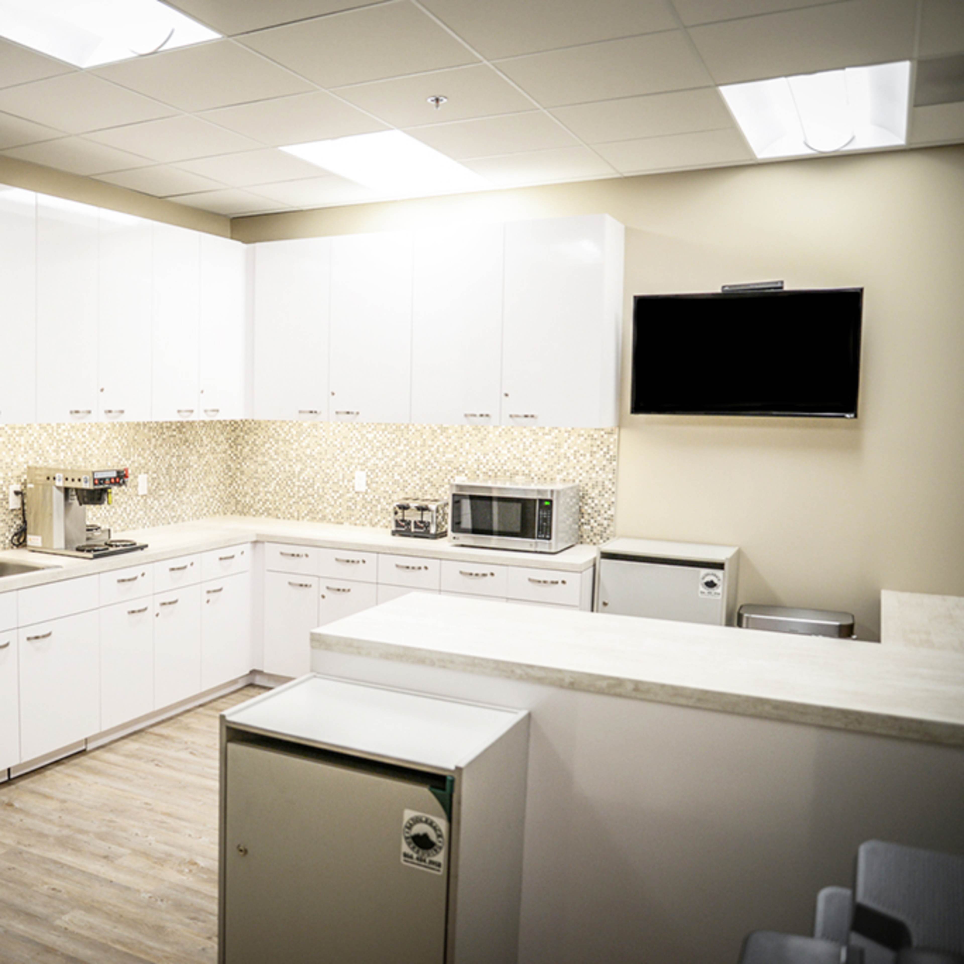 A modern kitchen with white cabinets, a stainless steel refrigerator, and a countertop equipped with various appliances.