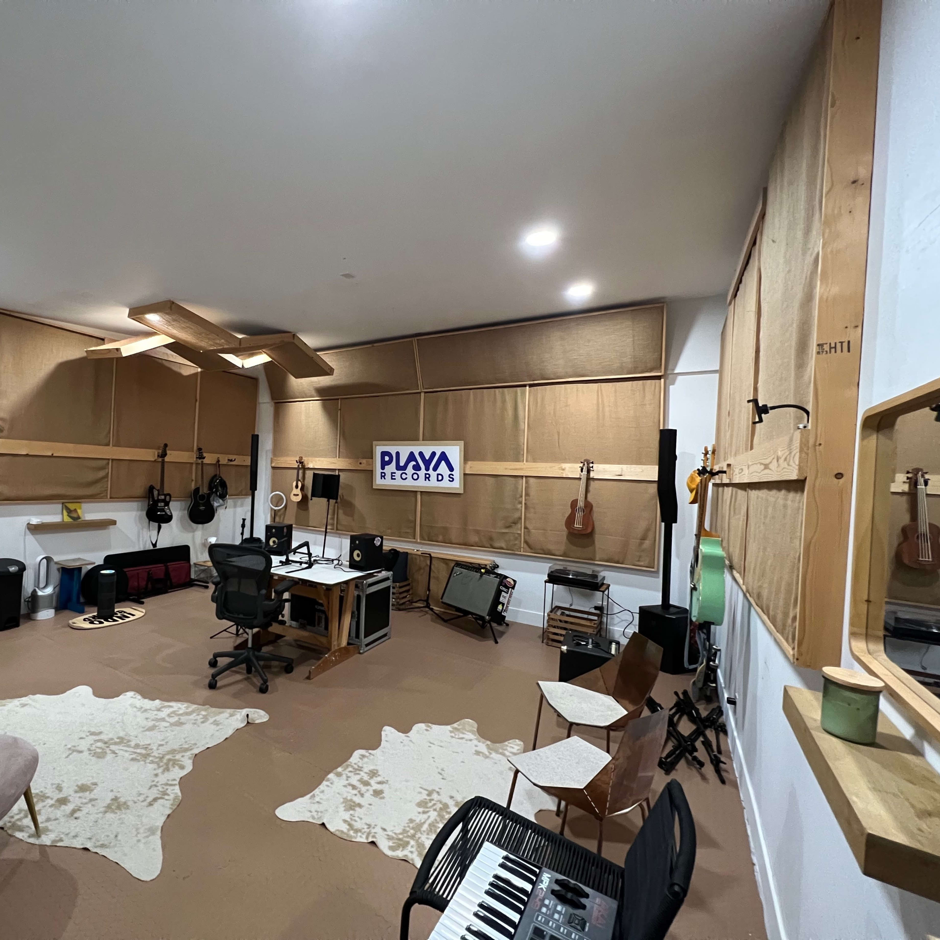 A music studio with various instruments, a large desk with equipment, and sound-absorbing panels on the walls.