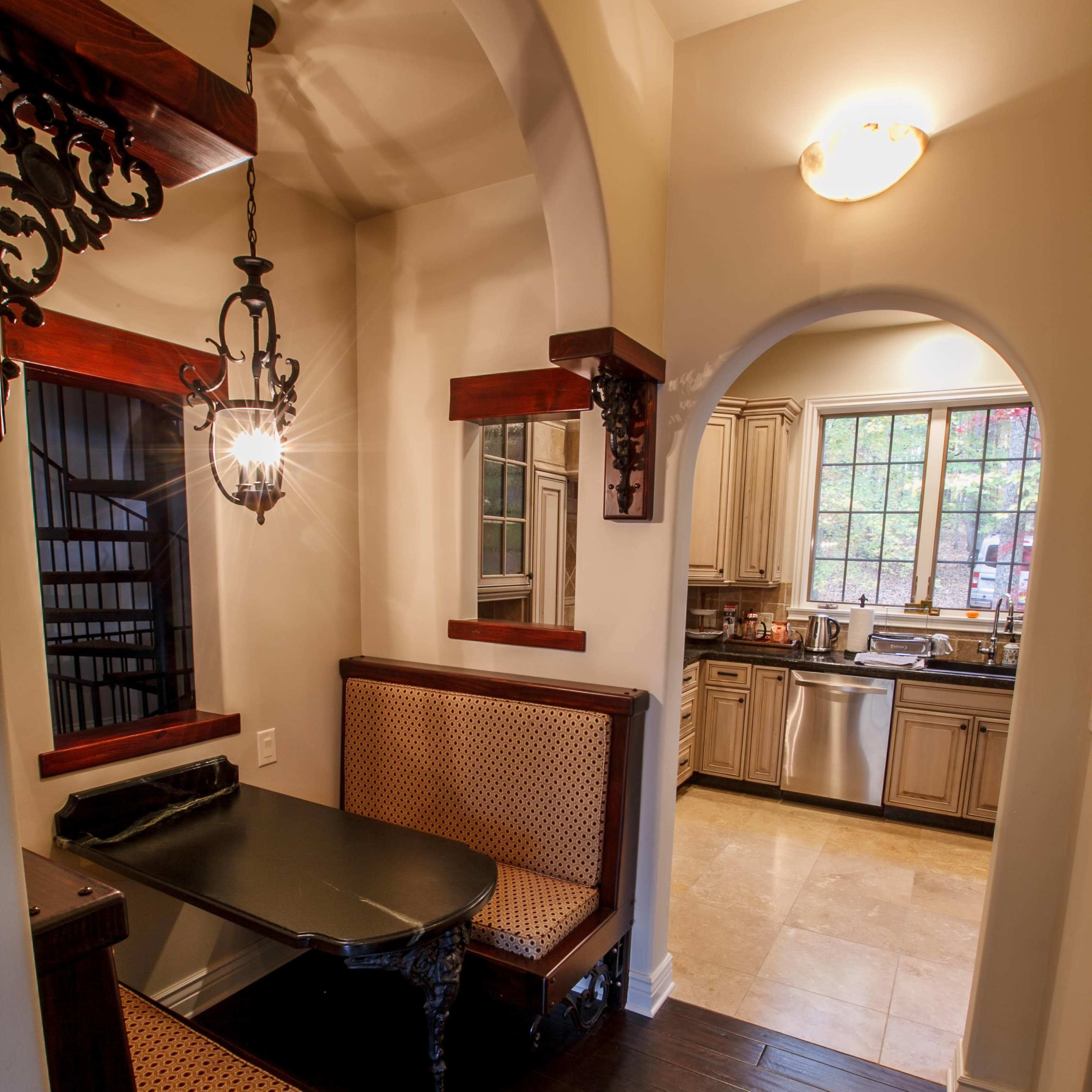 A small dining nook with a table and upholstered seating, leading to a kitchen visible through an arched entryway.