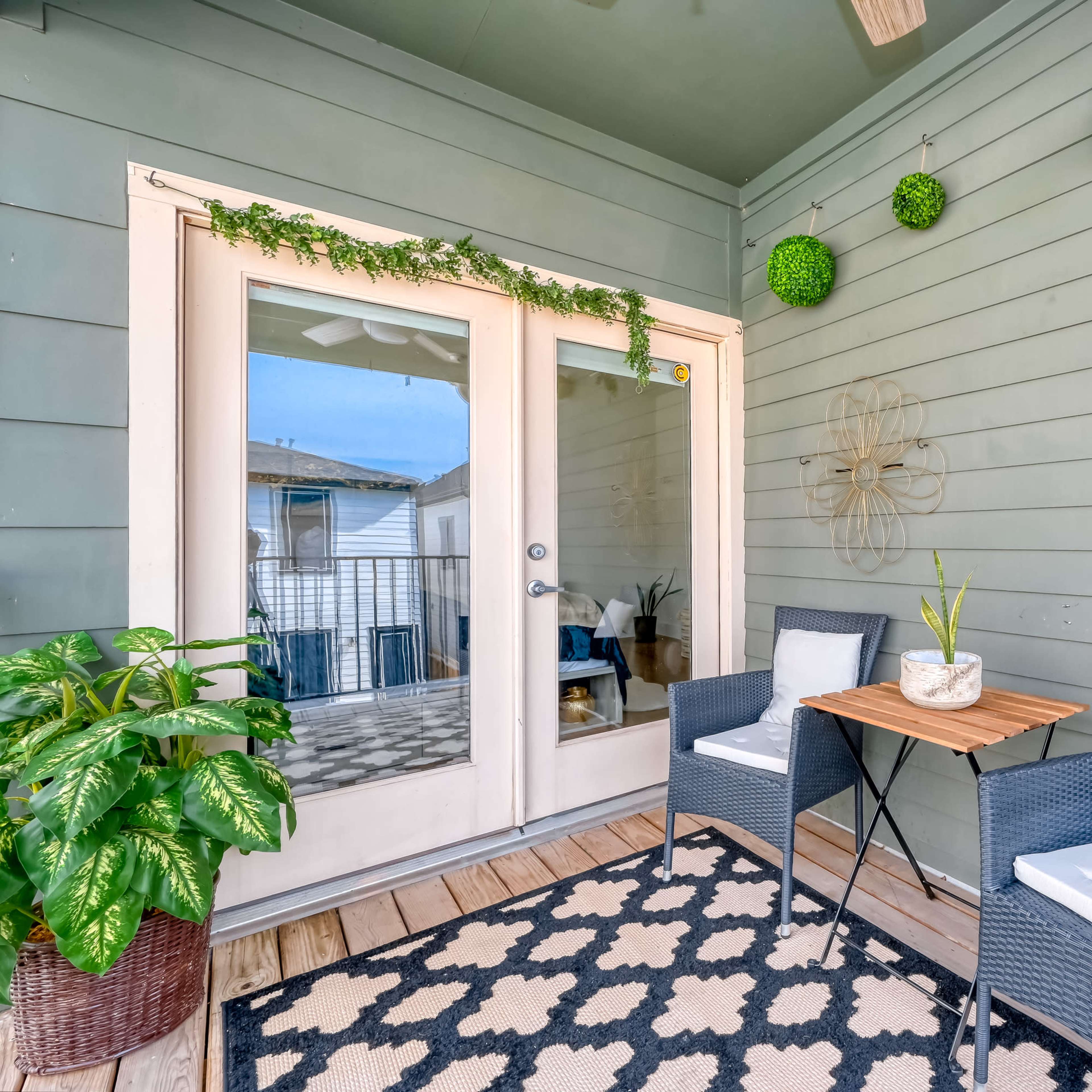 A small outdoor seating area with two chairs, a small table, and decorative plants against a green wooden wall.