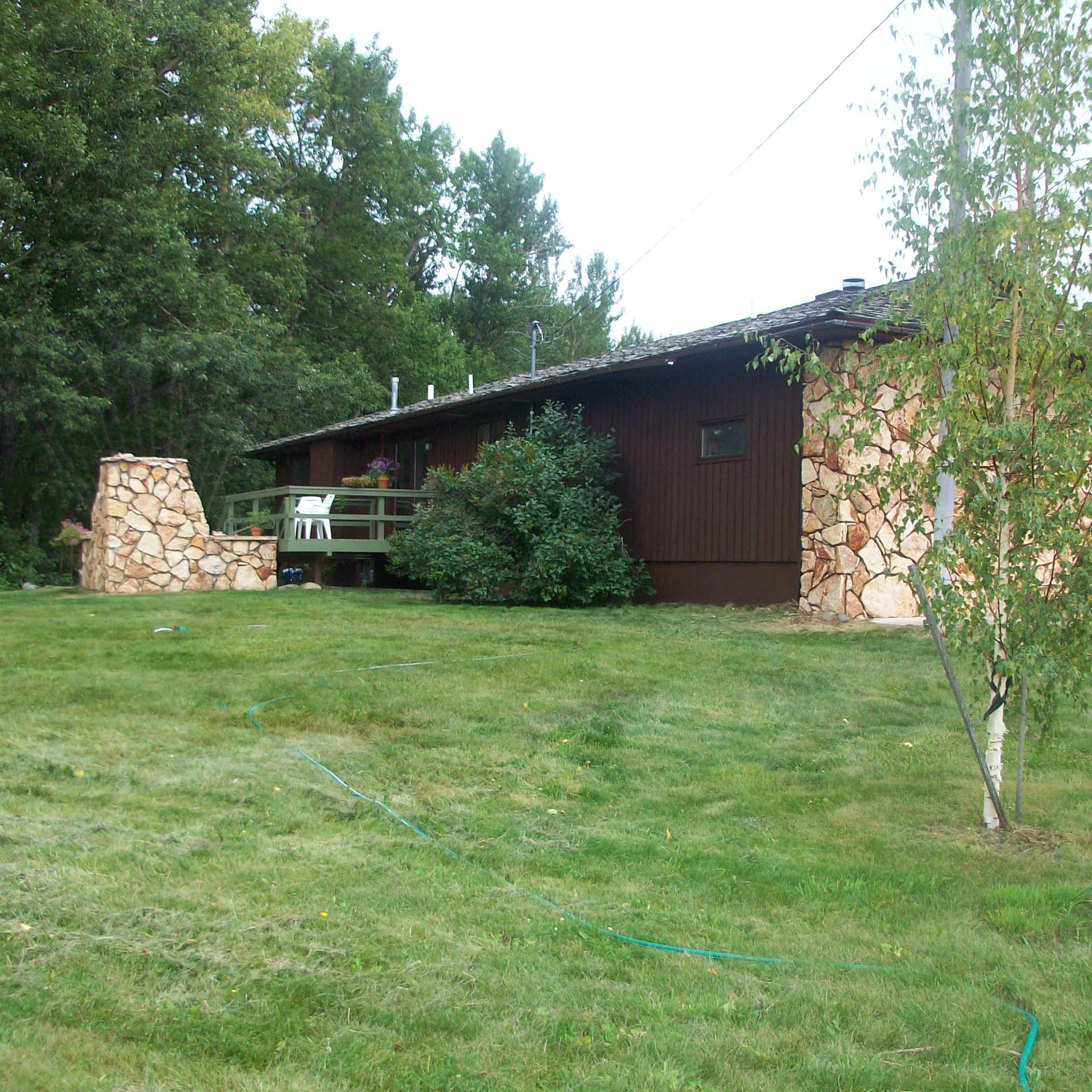 A single-story house with a stone and wood exterior is surrounded by lush greenery and a well-maintained lawn.