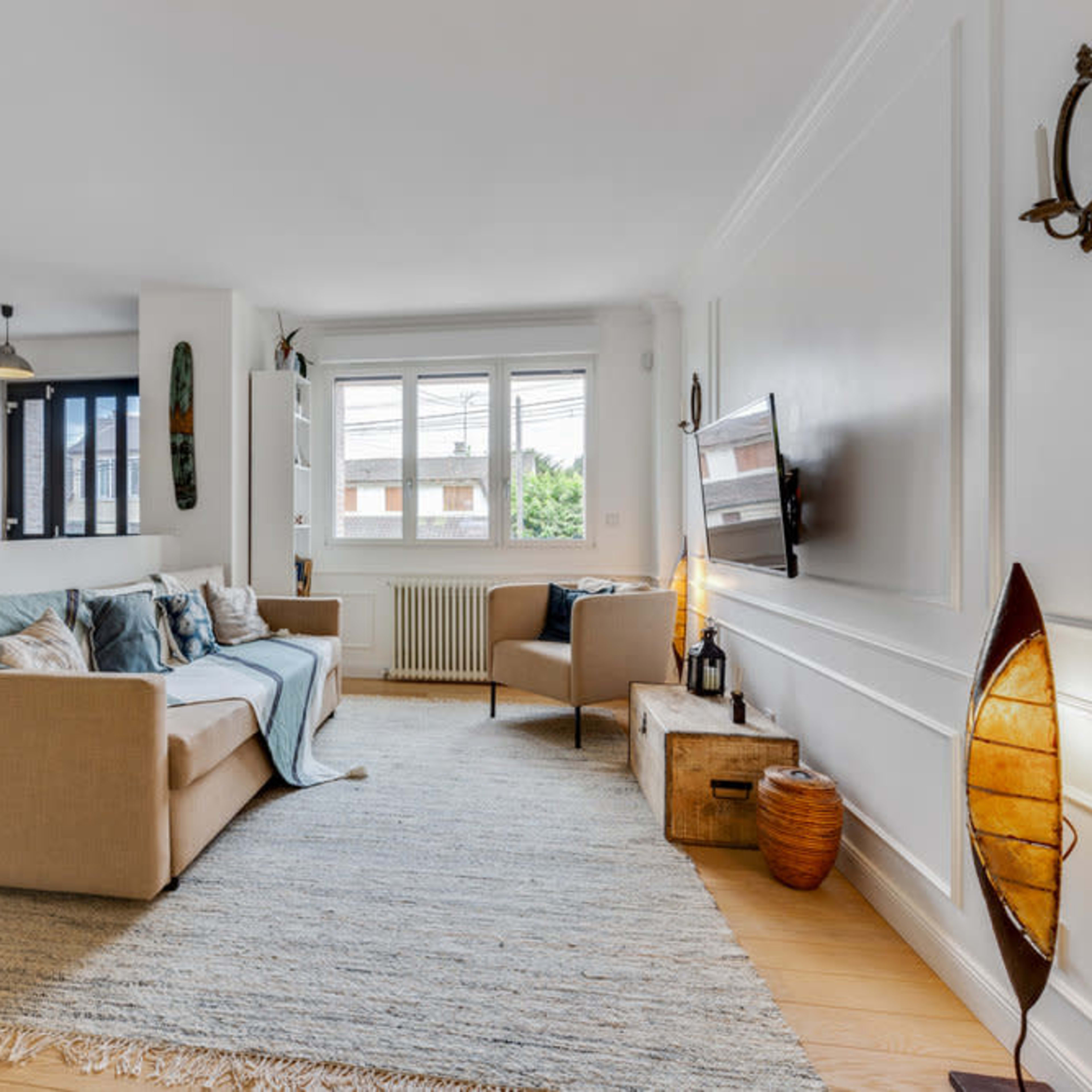 A light and airy living room features a beige sofa, a wooden armchair, and a decorative rug on a hardwood floor.