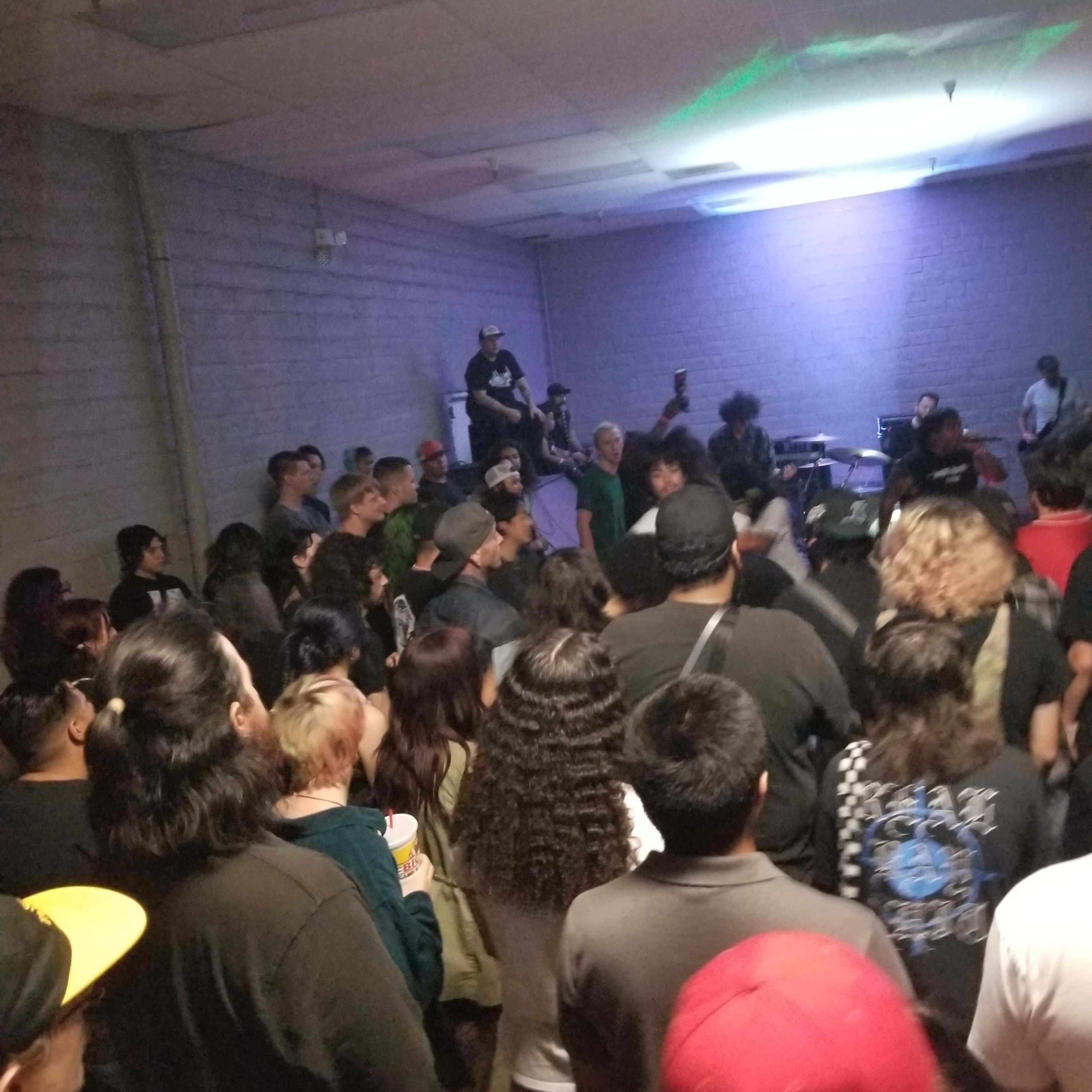 A crowd of people is gathered in a dimly lit room, watching a live band perform on stage.