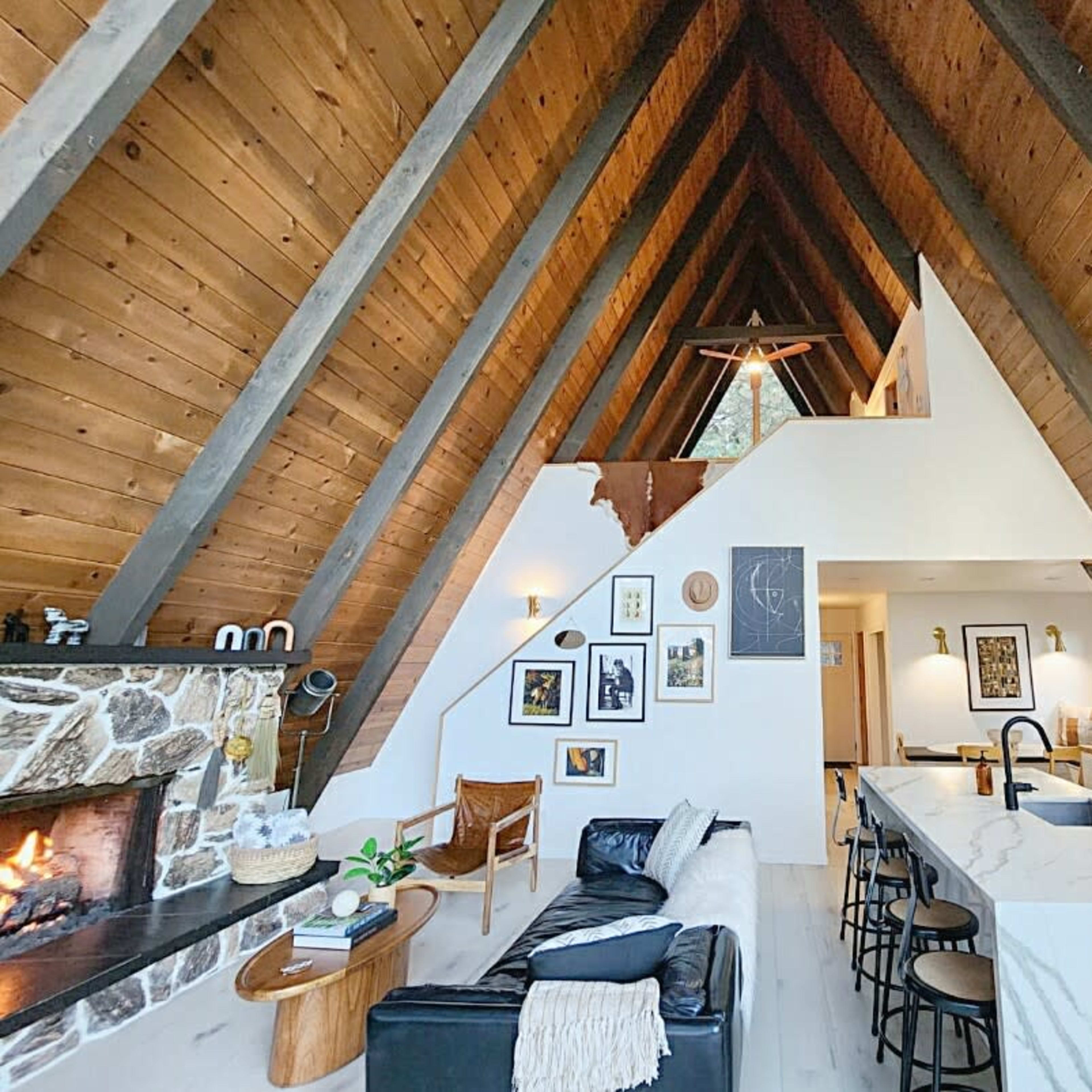 The interior of a spacious A-frame house features a stone fireplace, a modern kitchen with marble countertops, and large windows allowing natural light to fill the room.