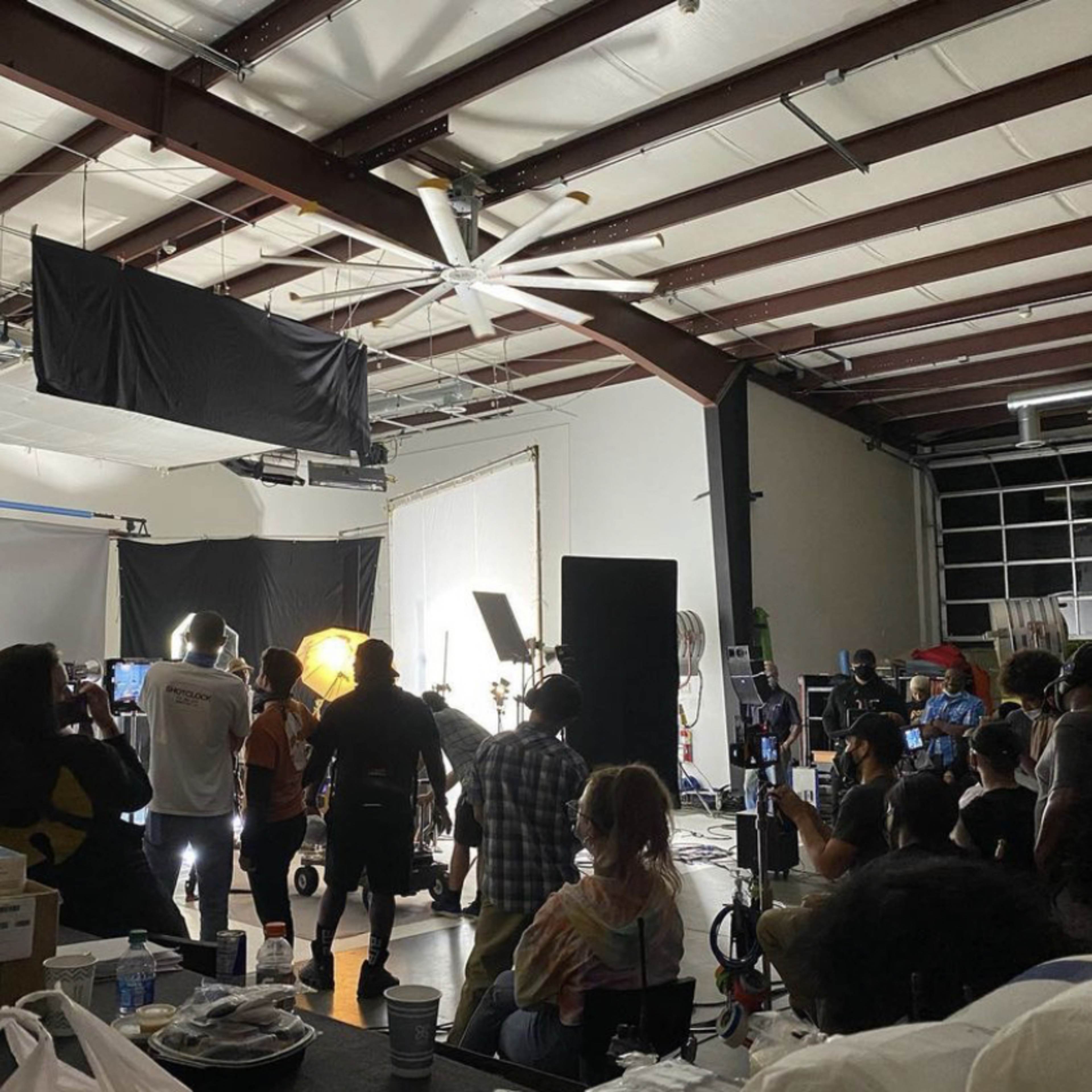 A film crew is working in a studio space with various lighting equipment and backdrops set up for a shoot.