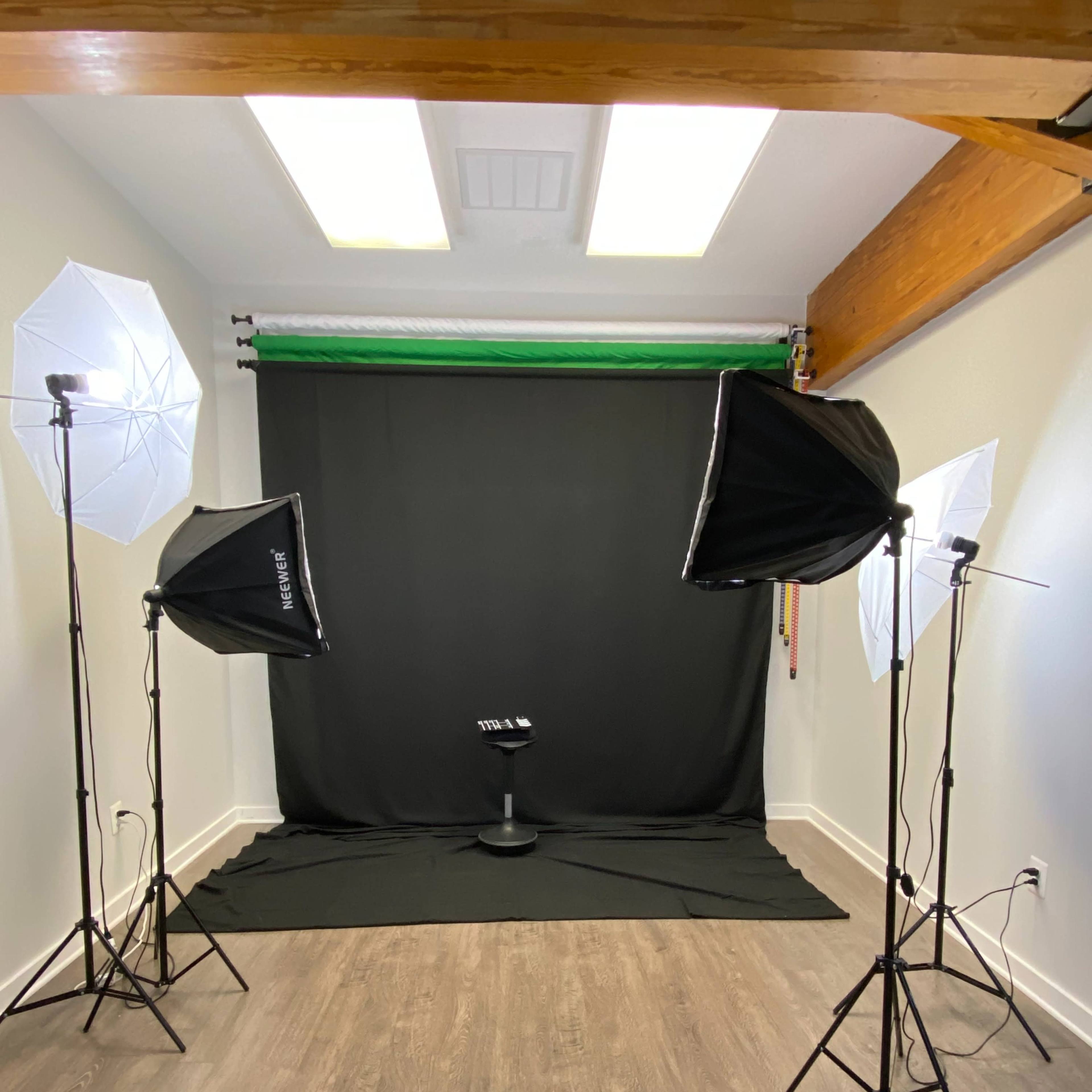 A photography studio setup with two softbox lights and a backdrop consisting of a black curtain and a green screen.
