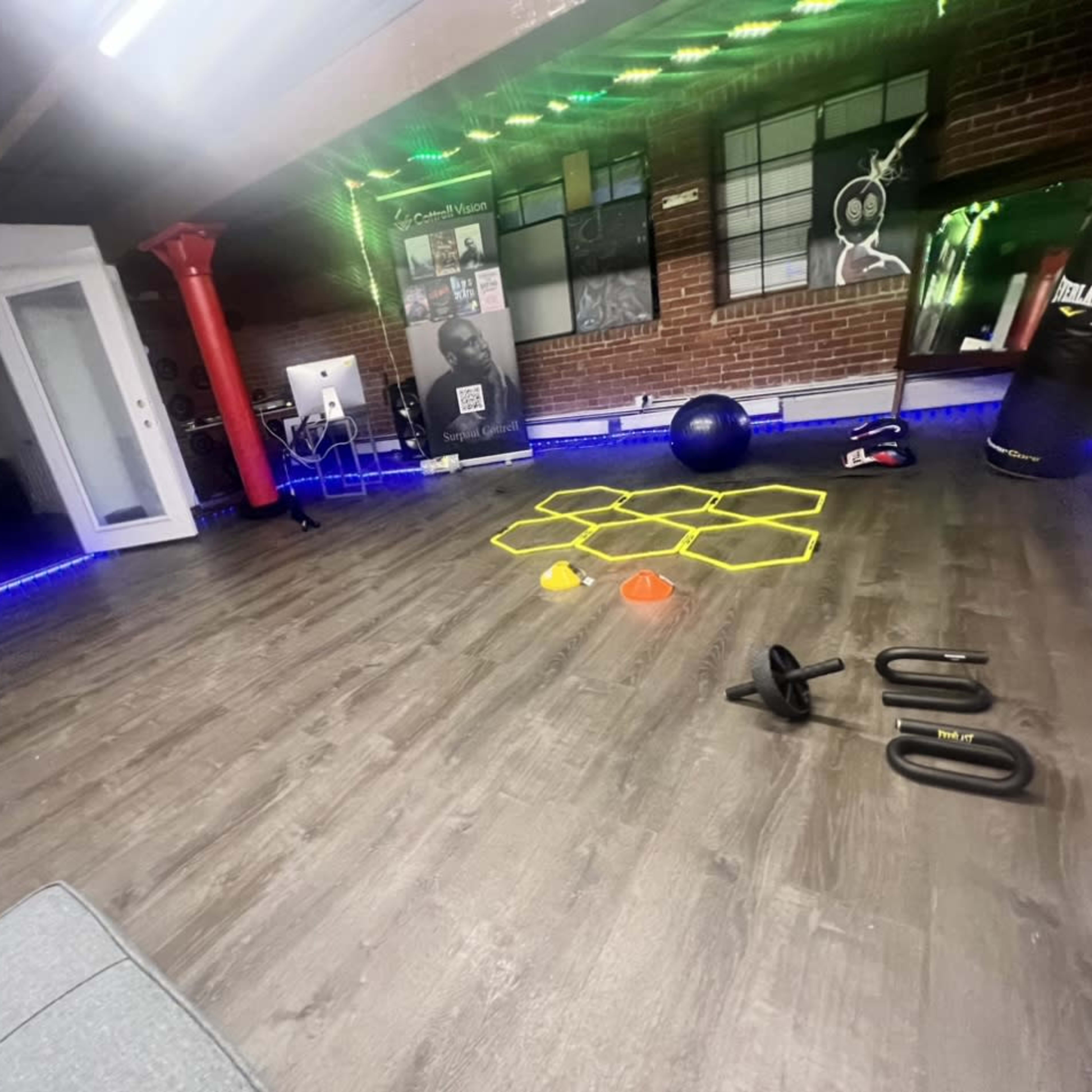 A fitness studio with exercise equipment, including weights, cones, and a stability ball, arranged on a wooden floor beneath colored lights.