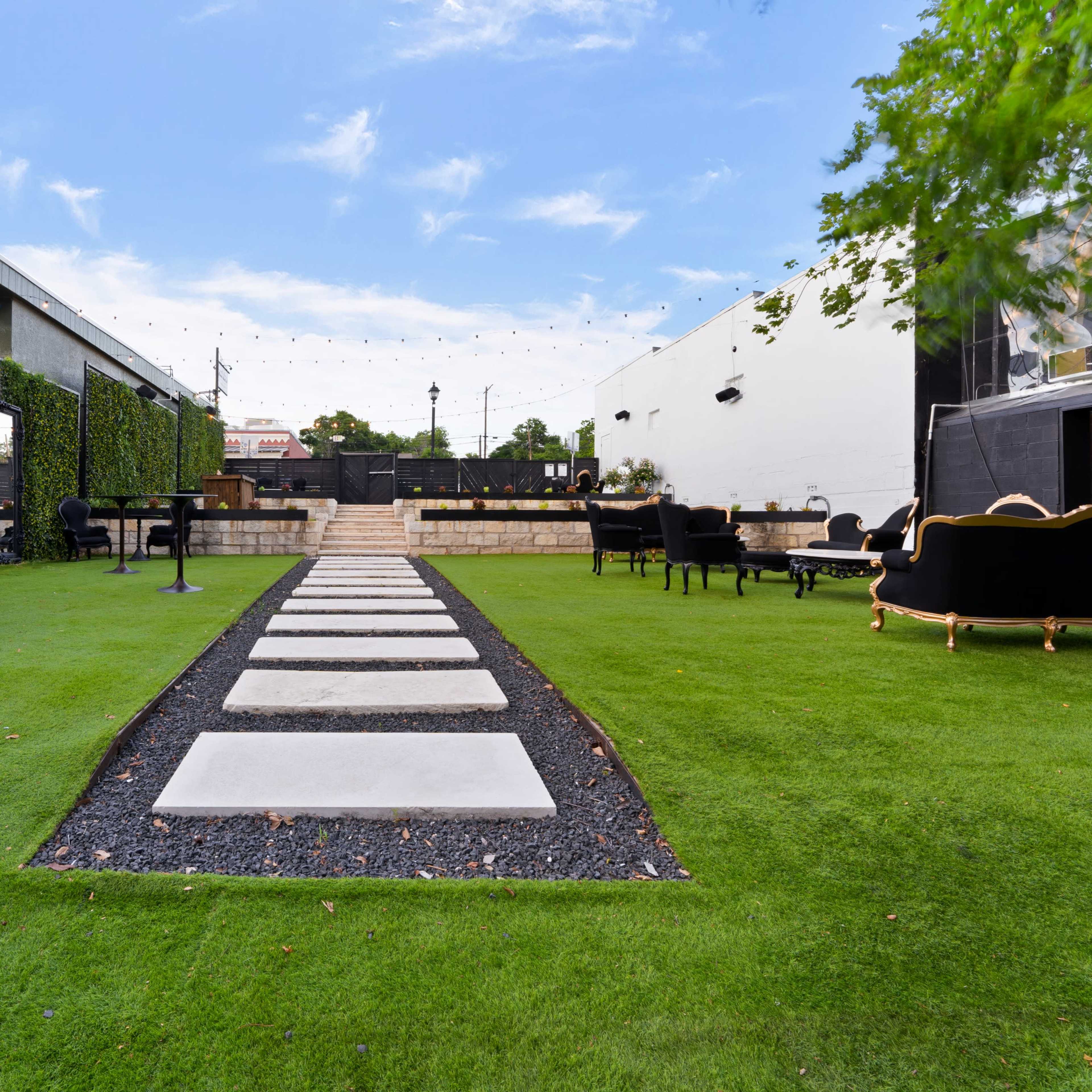 A pathway of stone slabs leads through a green lawn, flanked by decorative walls and seating areas.