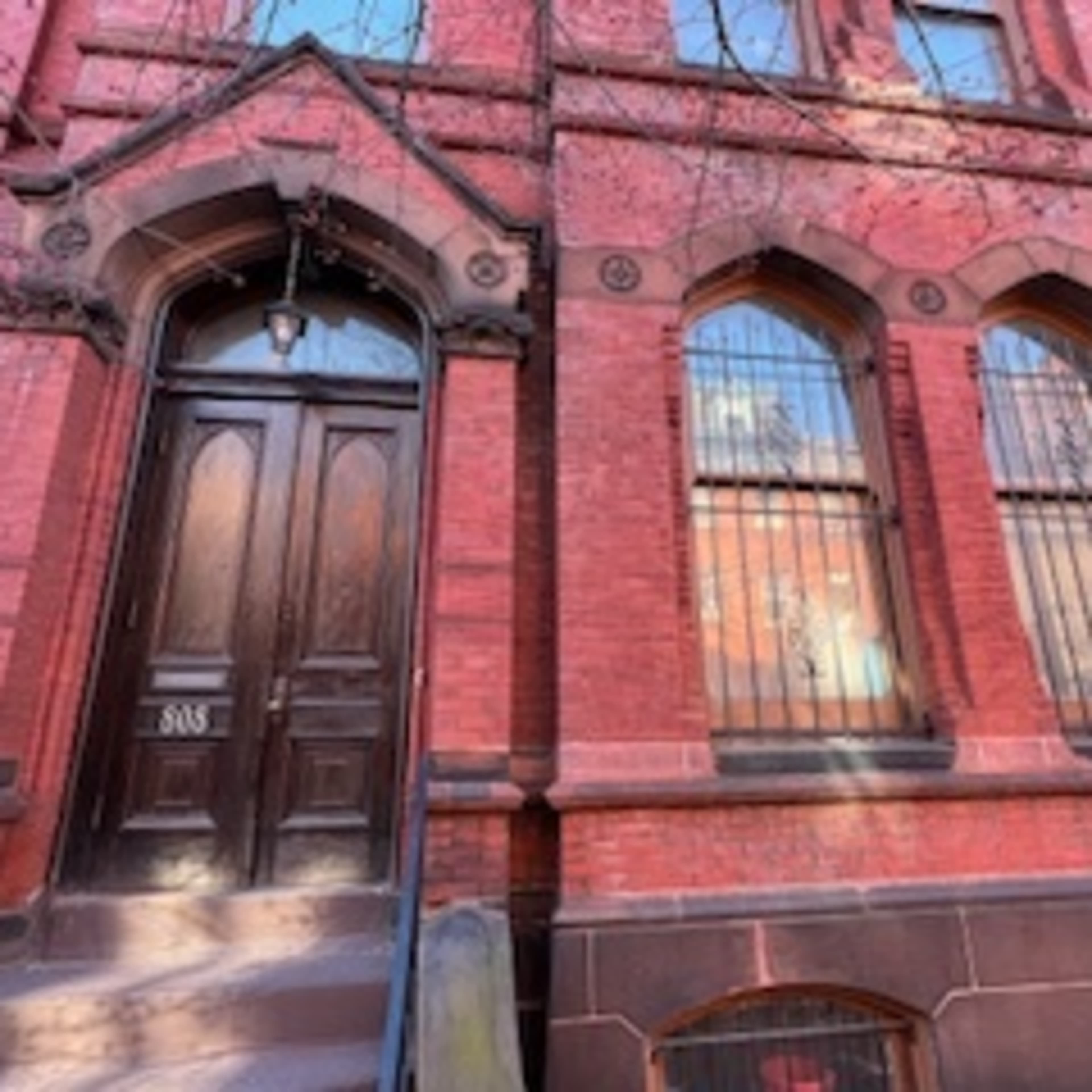 The entrance of a brick building with a wooden door and barred windows.