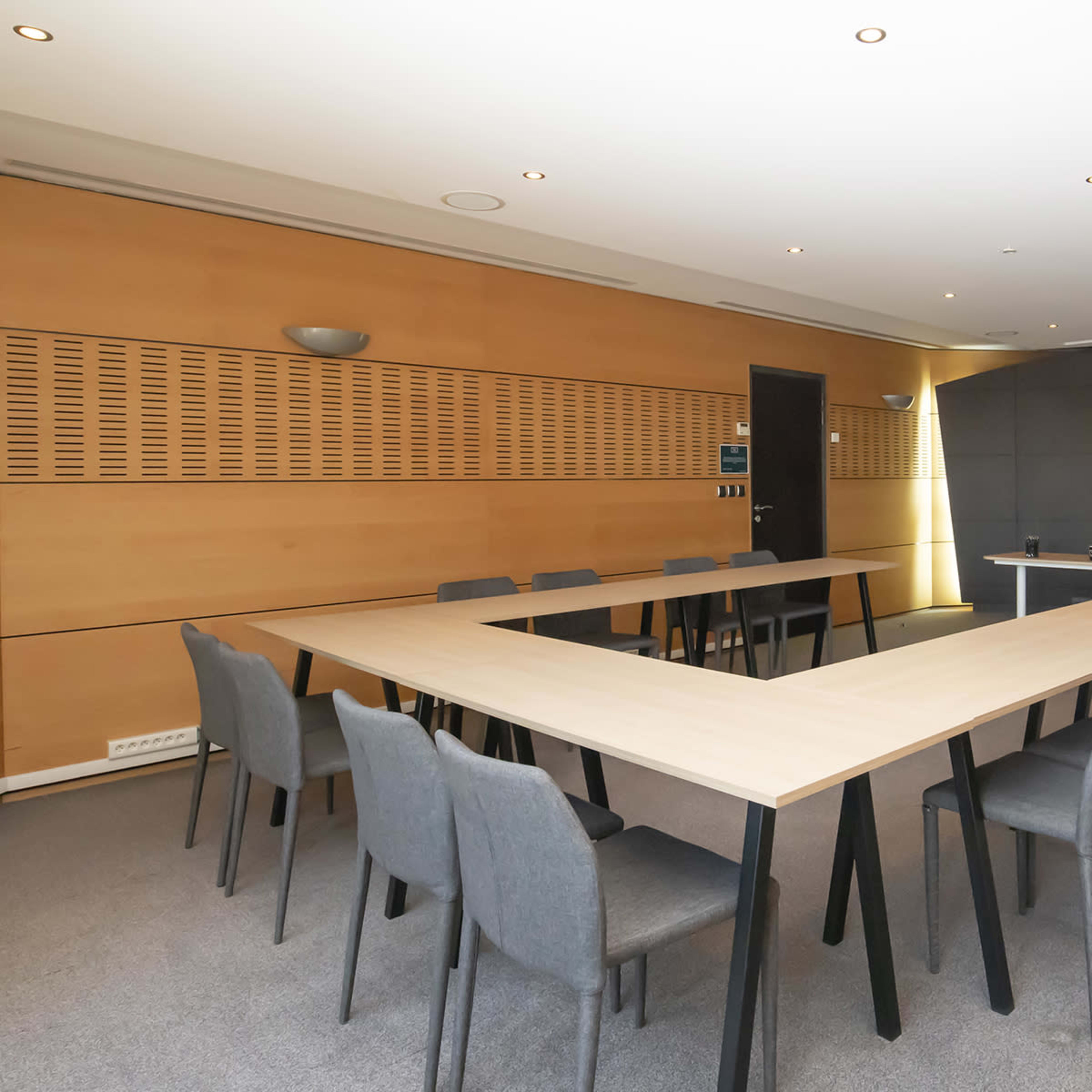 A conference room with a large, rectangular table surrounded by chairs, and a black wall with decorative elements at the end of the room.