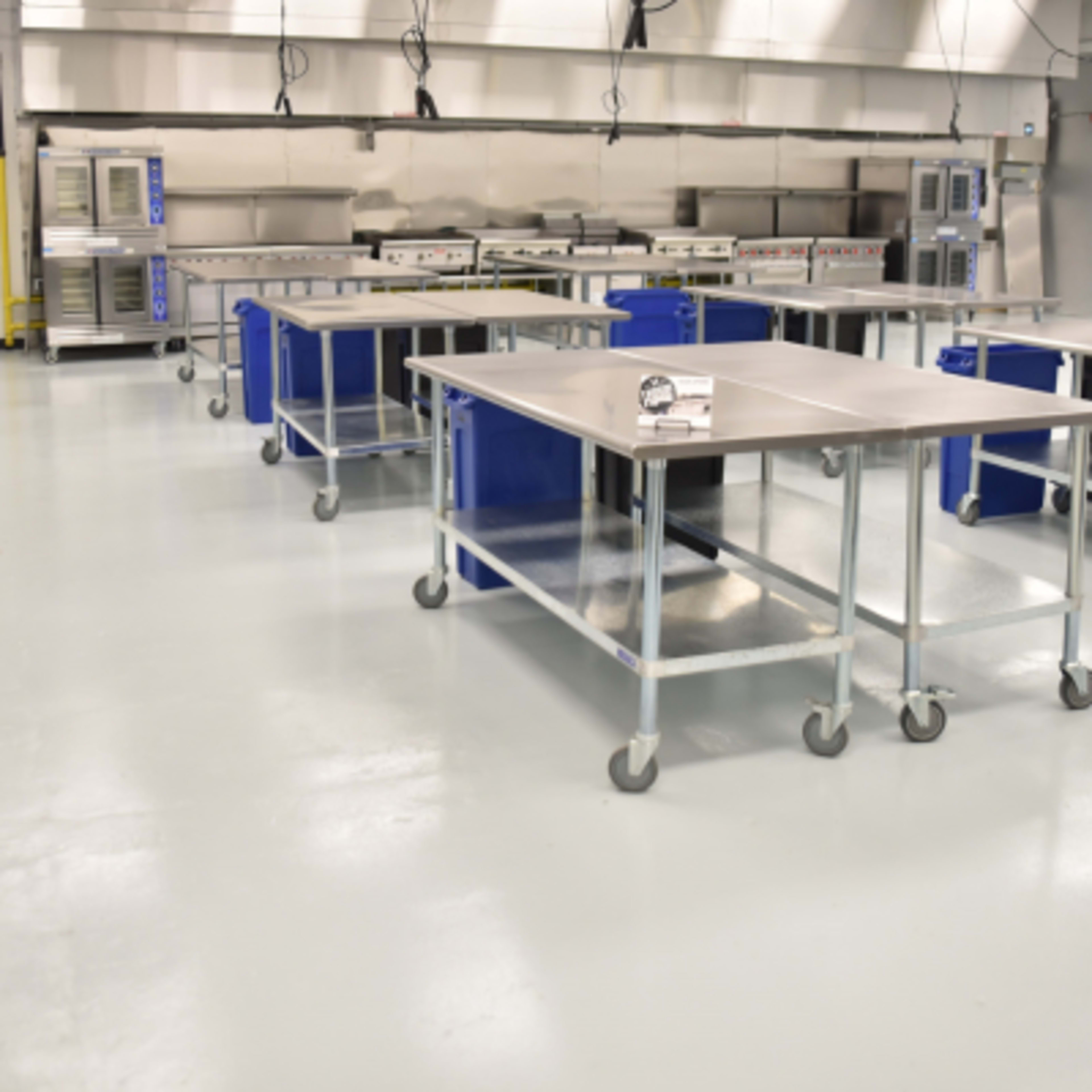 A spacious, industrial kitchen with stainless steel tables on wheels and a series of ovens in the background.