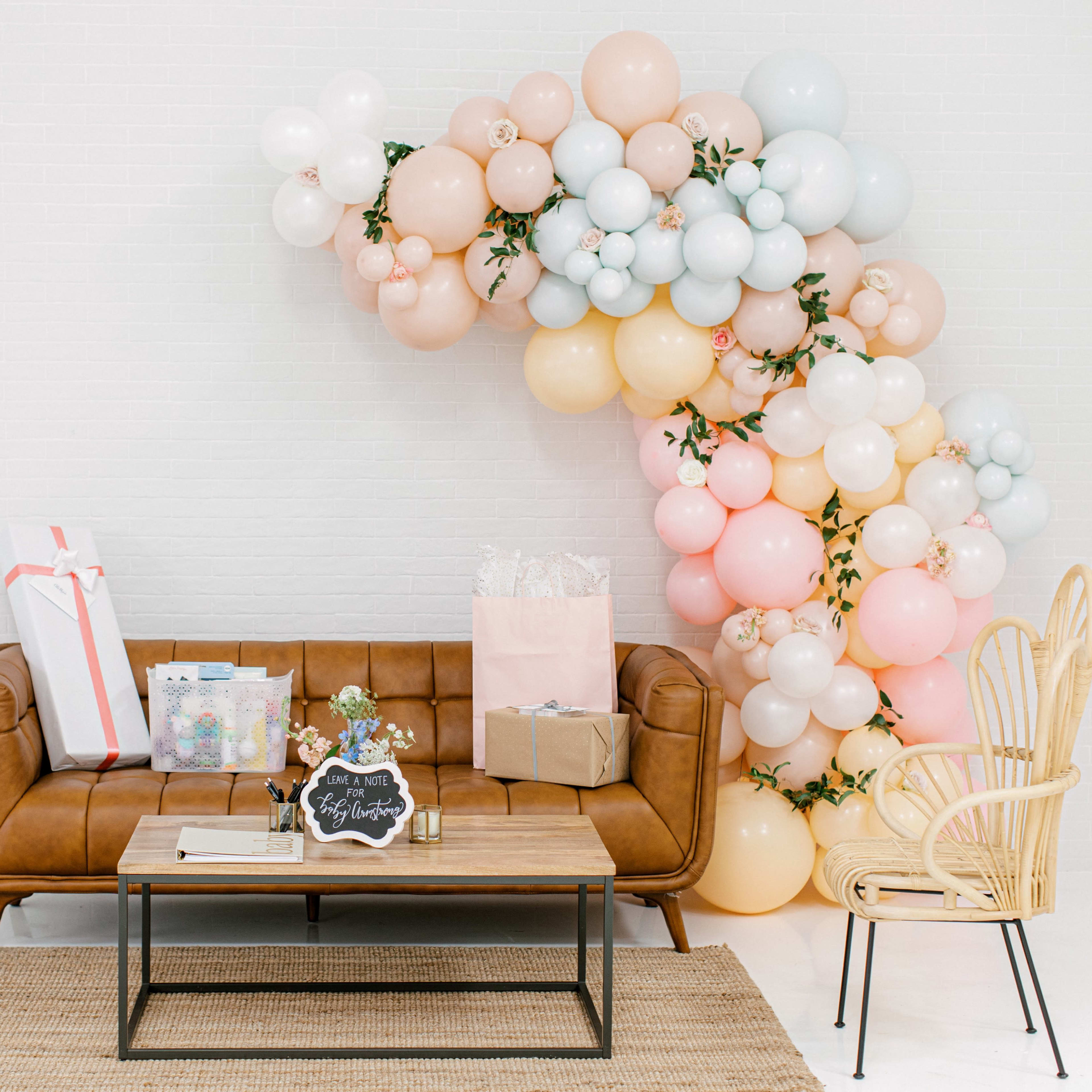 A brown leather sofa is positioned in front of a table, with a colorful balloon arch and gift packages on the floor beside it.