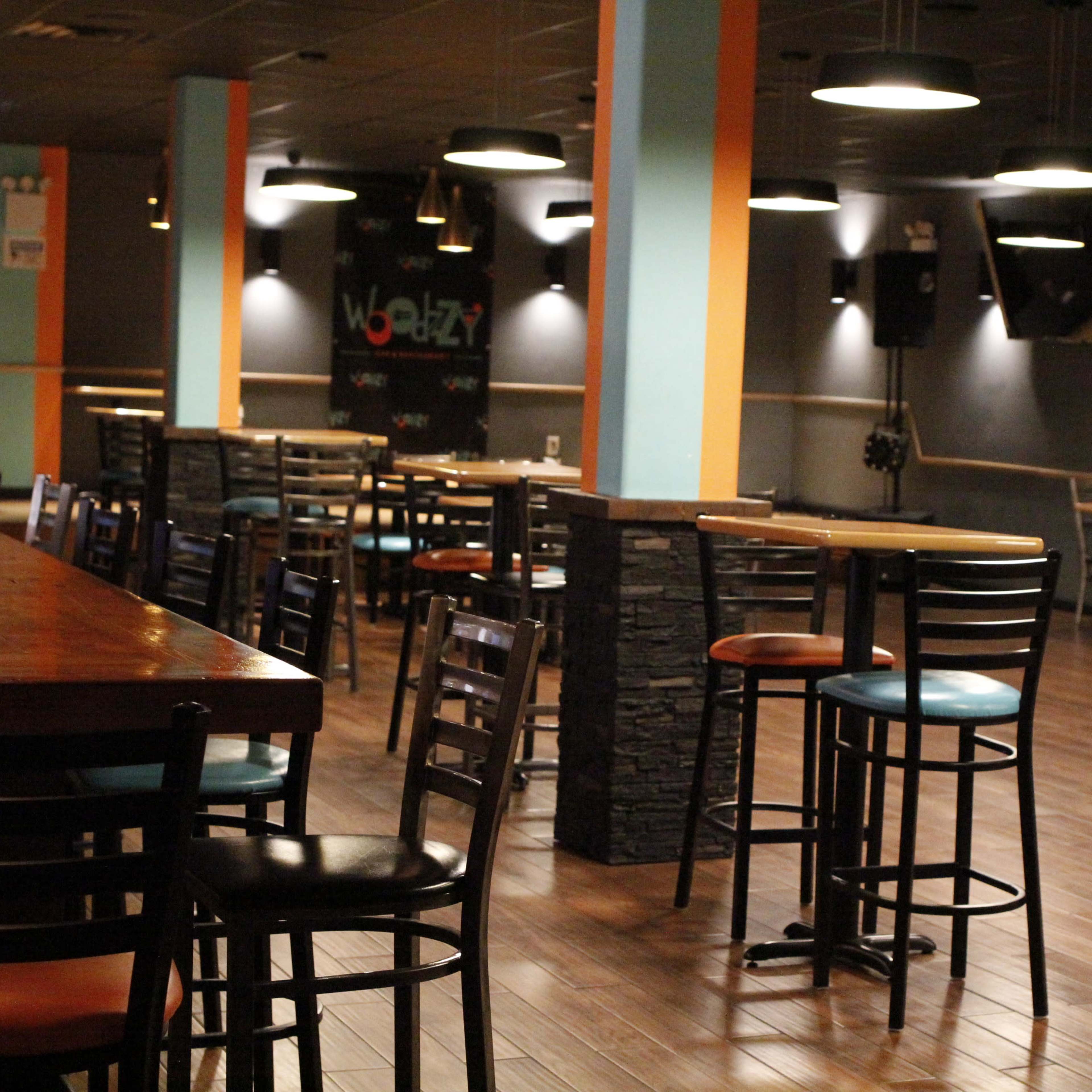 An empty bar area with wooden tables and black chairs arranged in a spacious, well-lit setting.