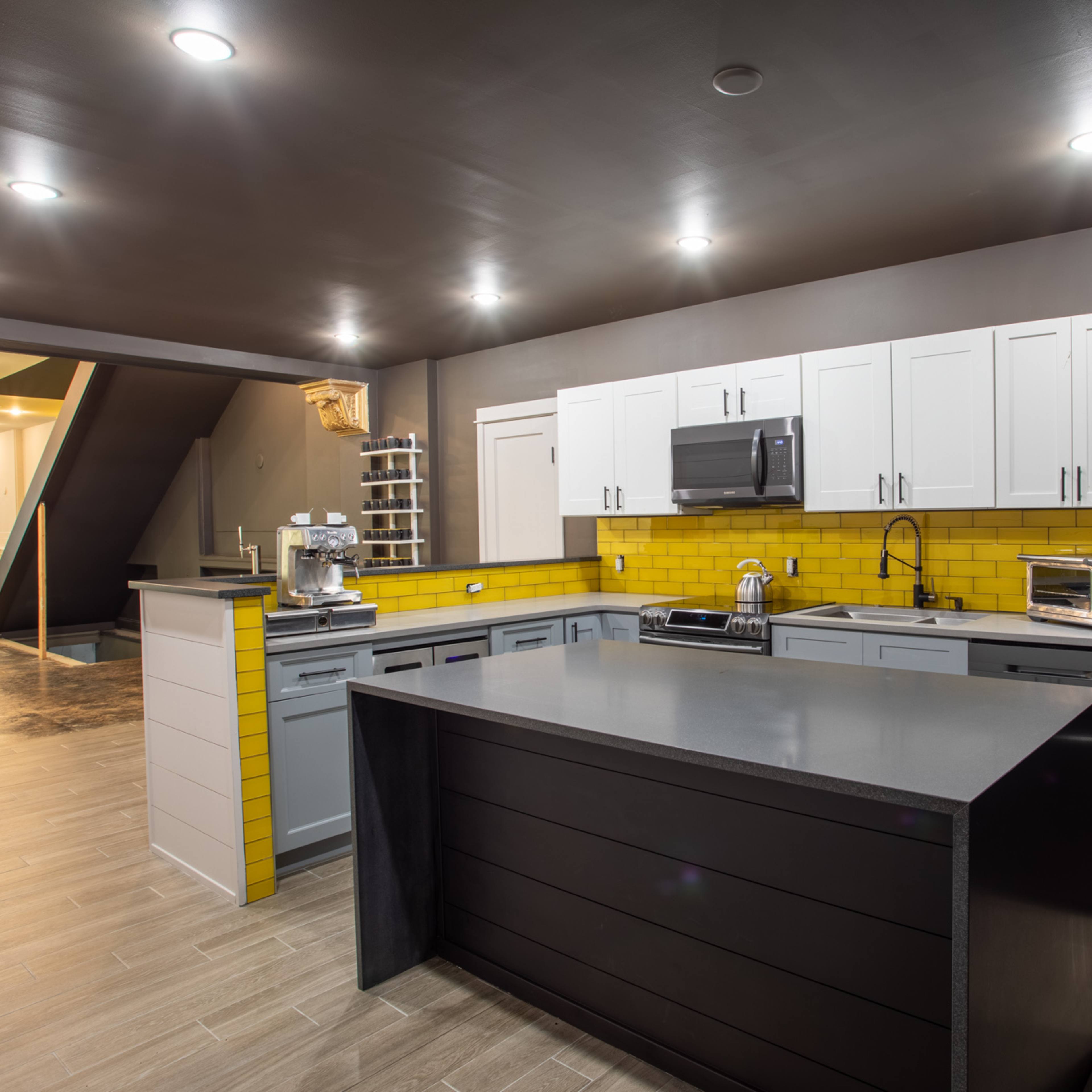 The kitchen features gray and white cabinetry, a black island, and a yellow tiled backsplash.