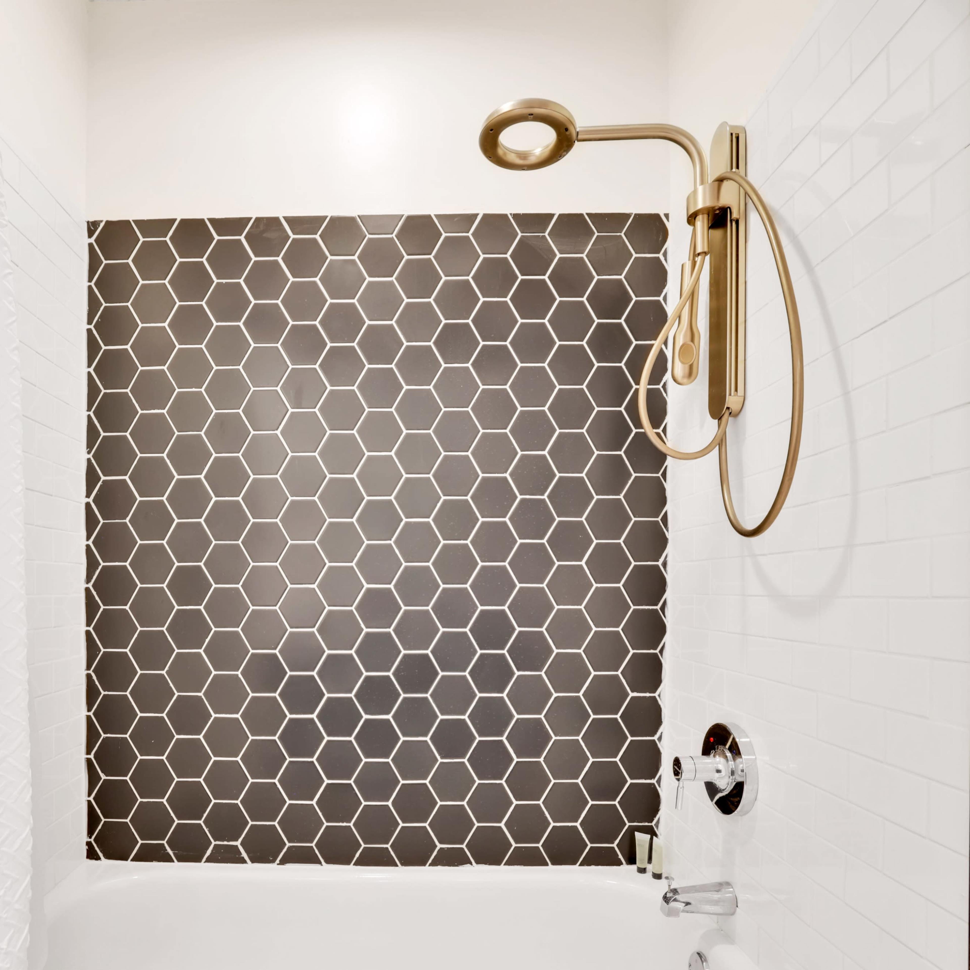 A shower area featuring a hexagonal patterned wall, a gold showerhead, and a white curtain.