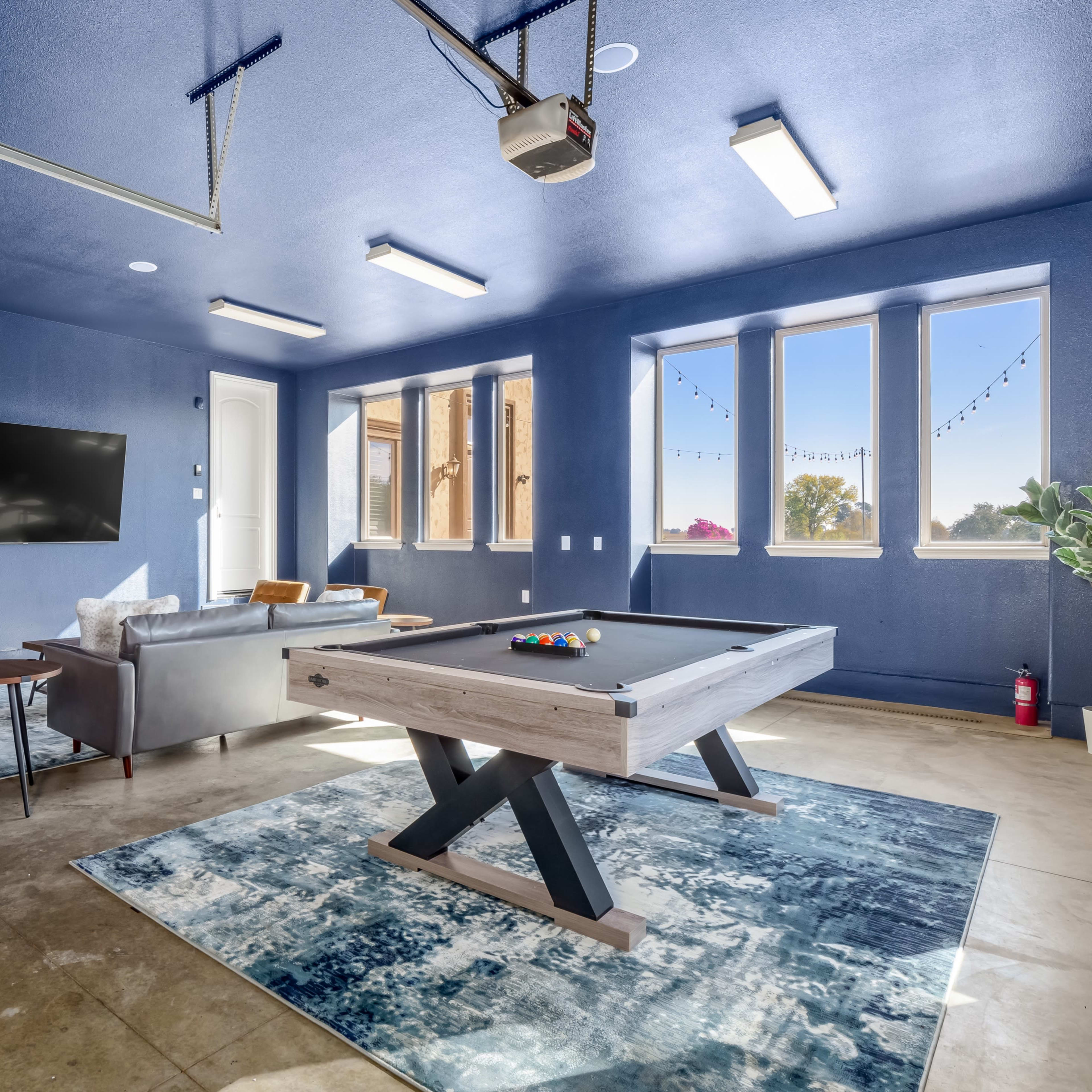 A spacious garage converted into a recreational room, featuring a pool table, seating area, and large windows.