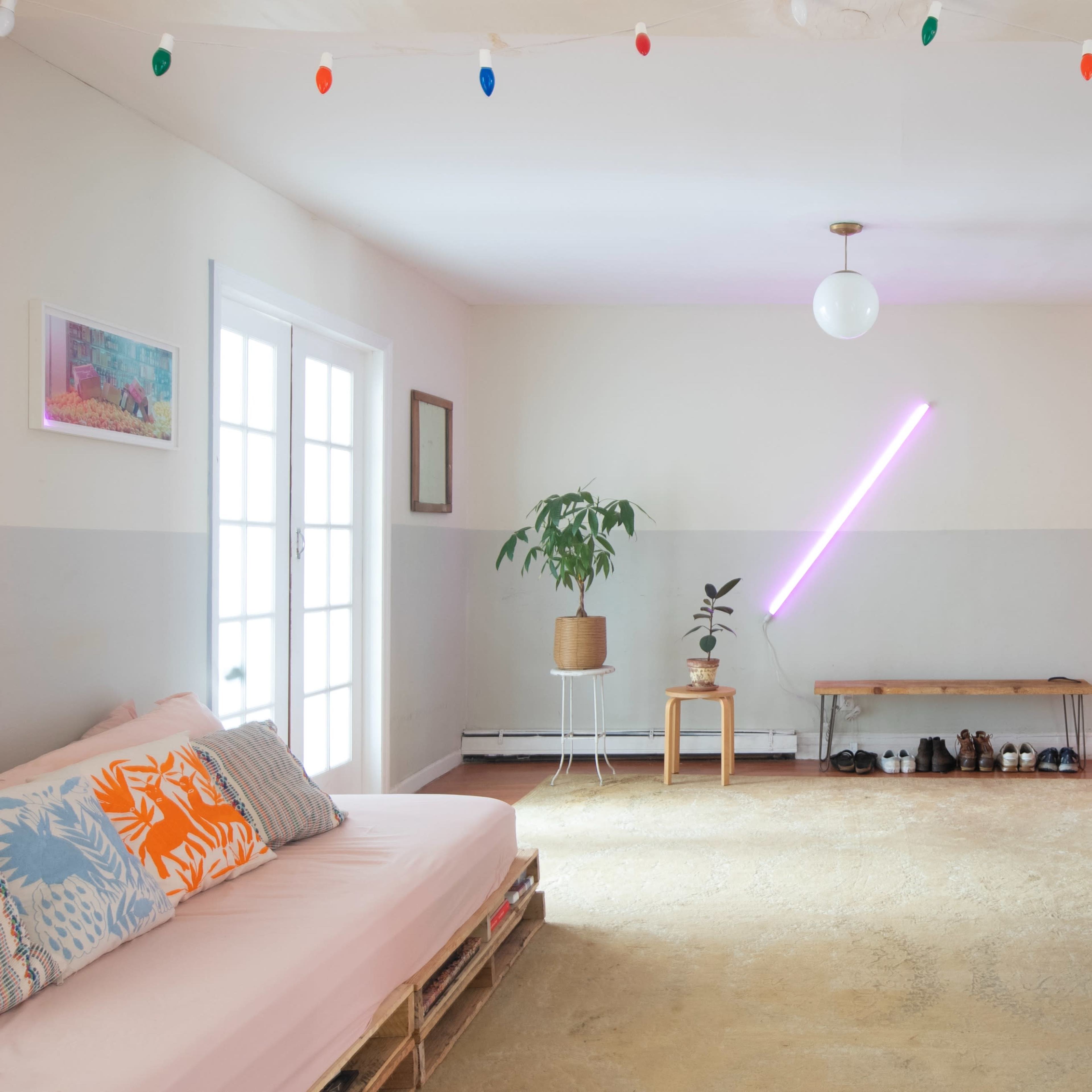 A bright living room features a minimalist design with a sofa, a bench, a plant, and a neon light on the wall.