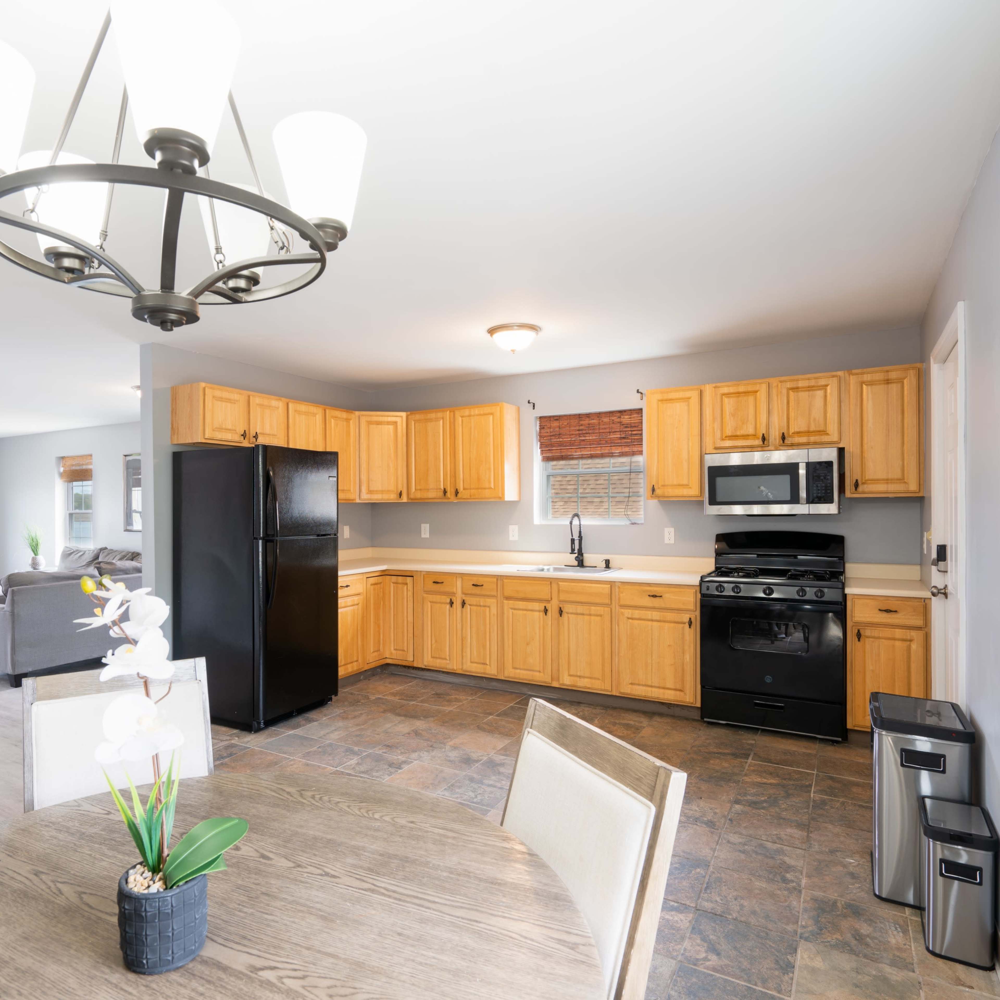 A kitchen with wooden cabinets, a black refrigerator, a stainless steel microwave, and a dining table with a plant centerpiece.