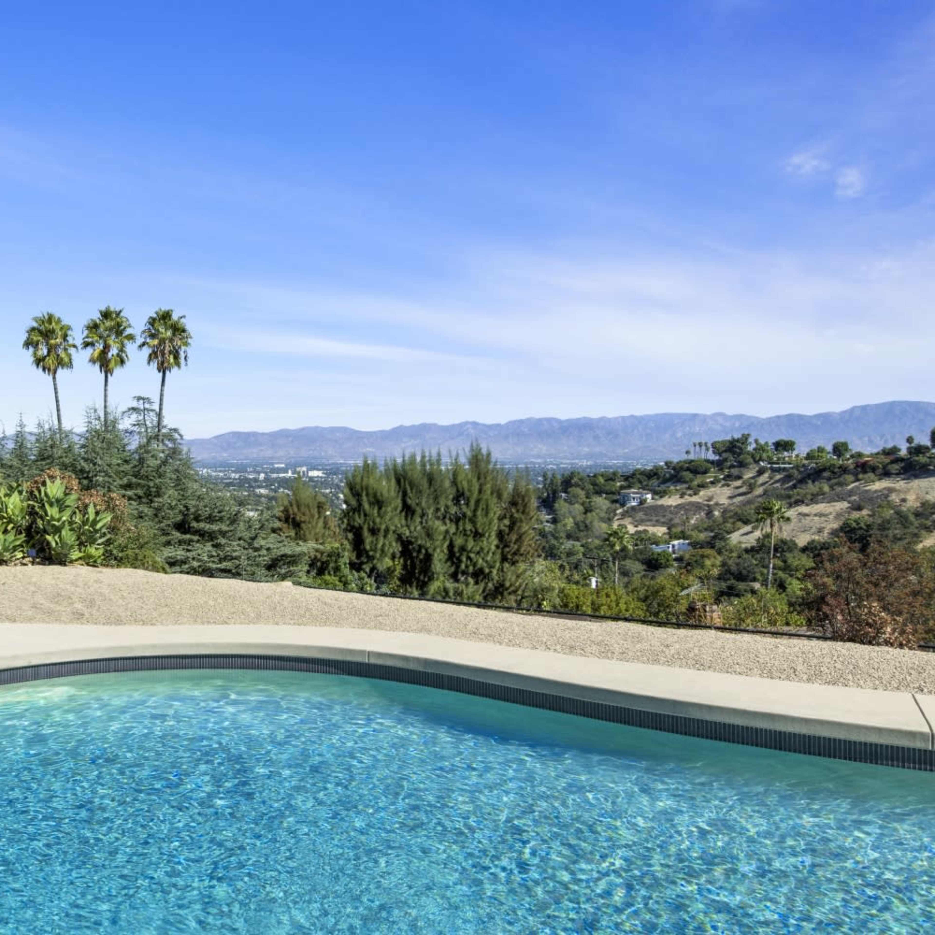 The interior space features large windows overlooking a pool area and a modern fireplace in a minimalist setting.