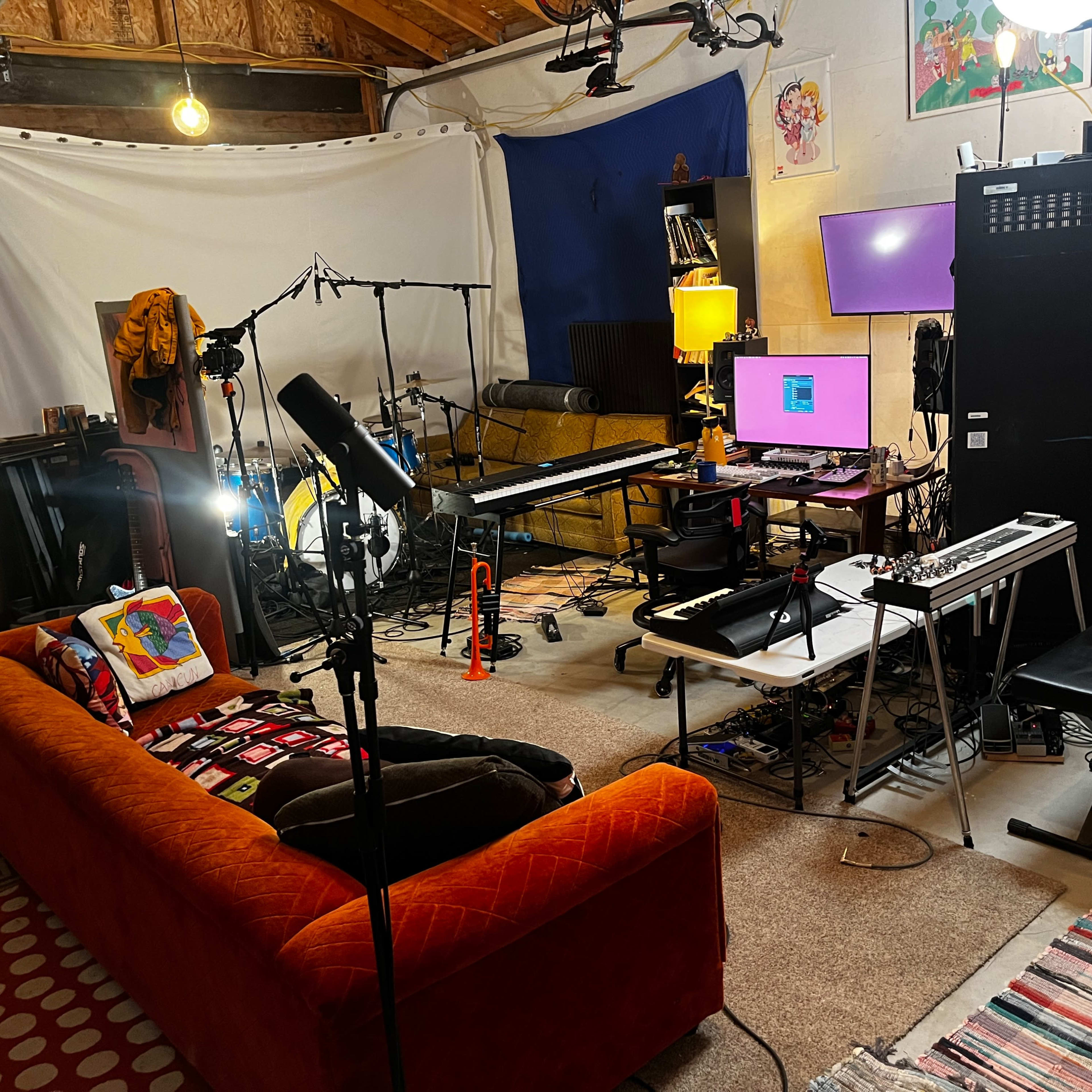 A music studio setup featuring a comfortable orange couch, musical instruments, recording equipment, and various lighting sources.