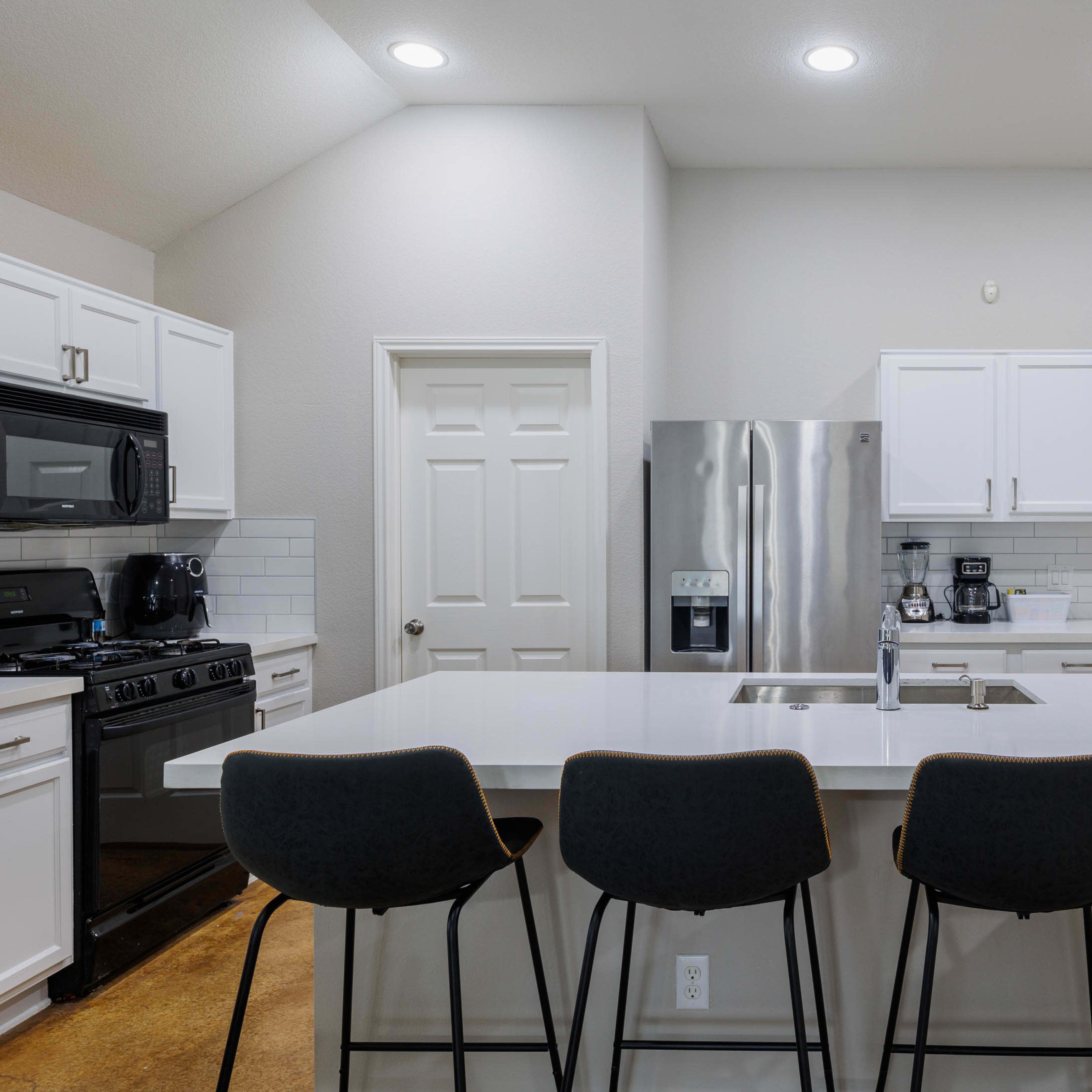 A modern kitchen features white cabinetry, stainless steel appliances, and a large island with four black bar stools.
