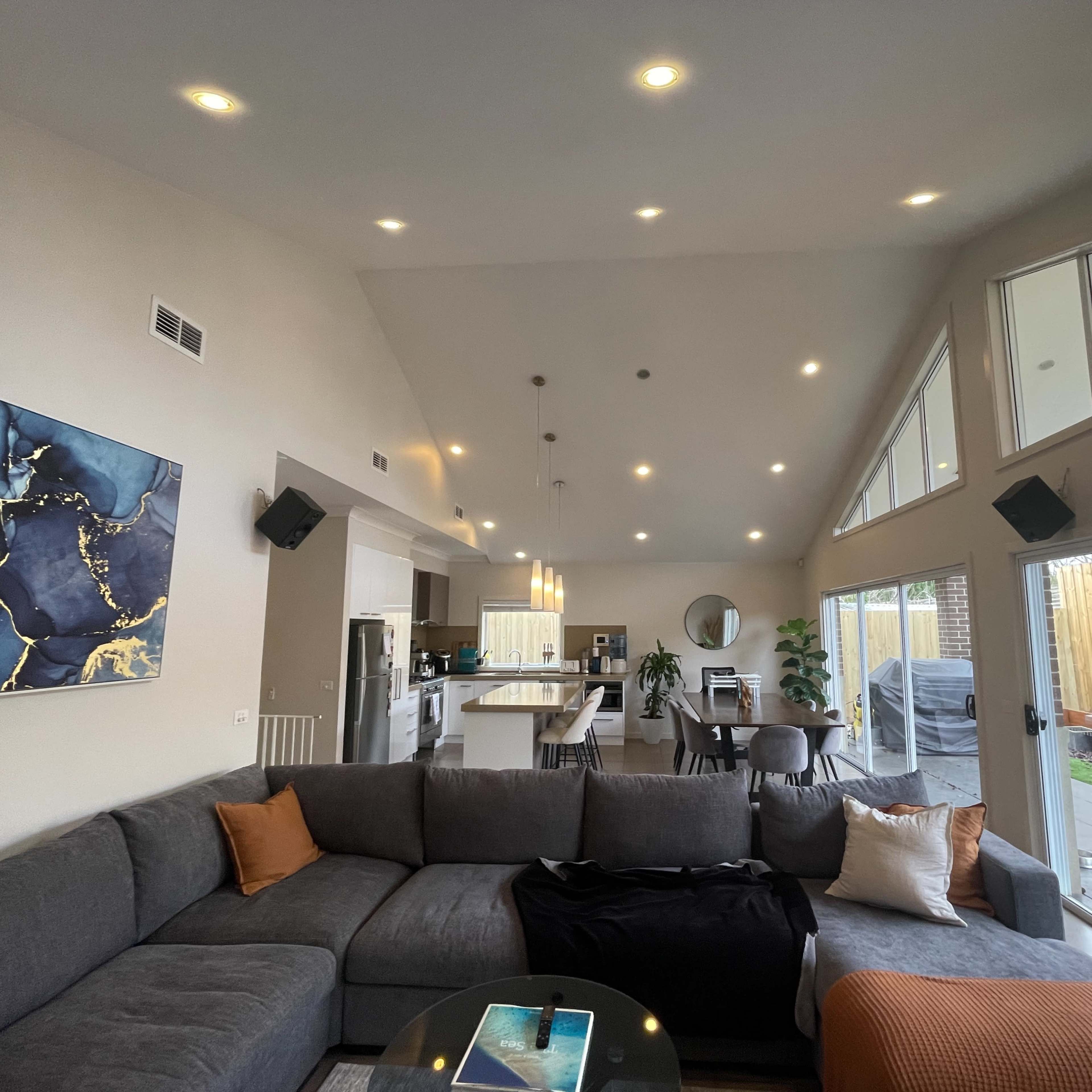 A modern living room with a large sectional sofa, a coffee table, and a view of an open kitchen and dining area, featuring large windows that let in natural light.