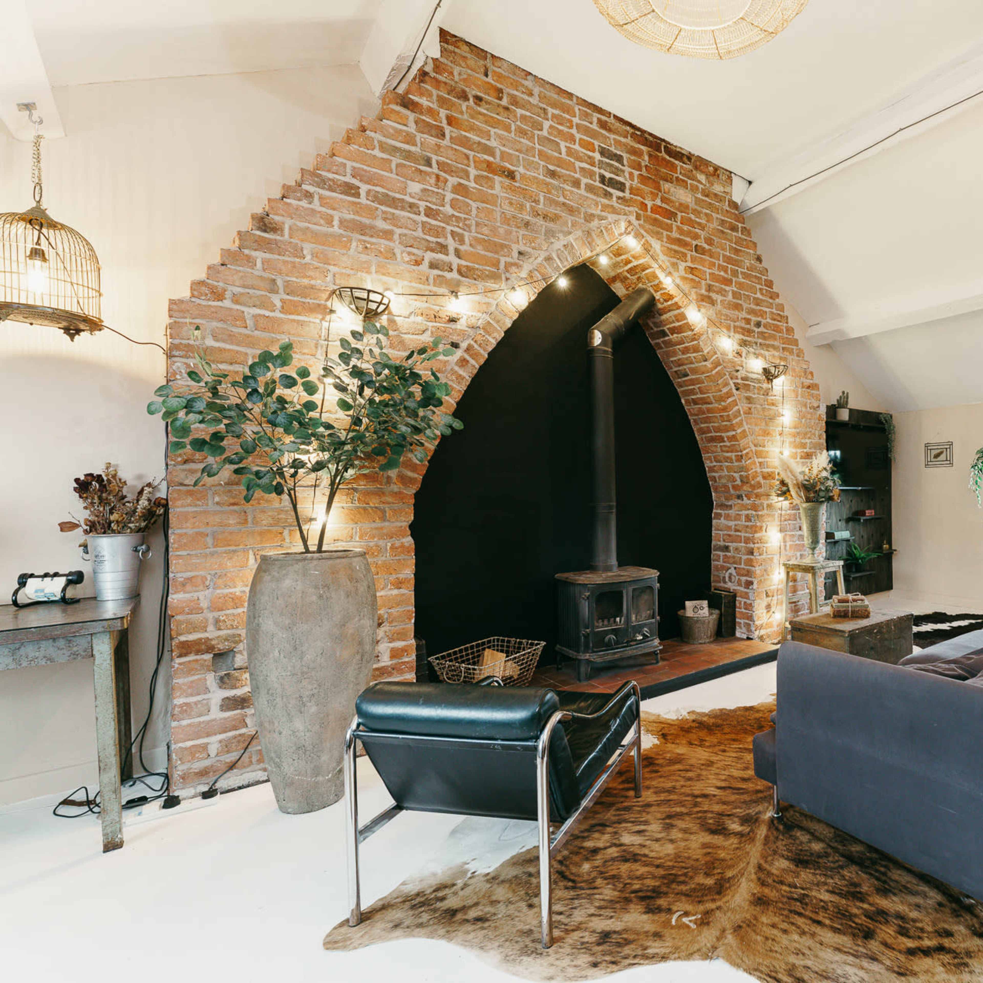 A living space with a large brick archway, a black wood stove, and a sofa arranged near a decorative cowhide rug.