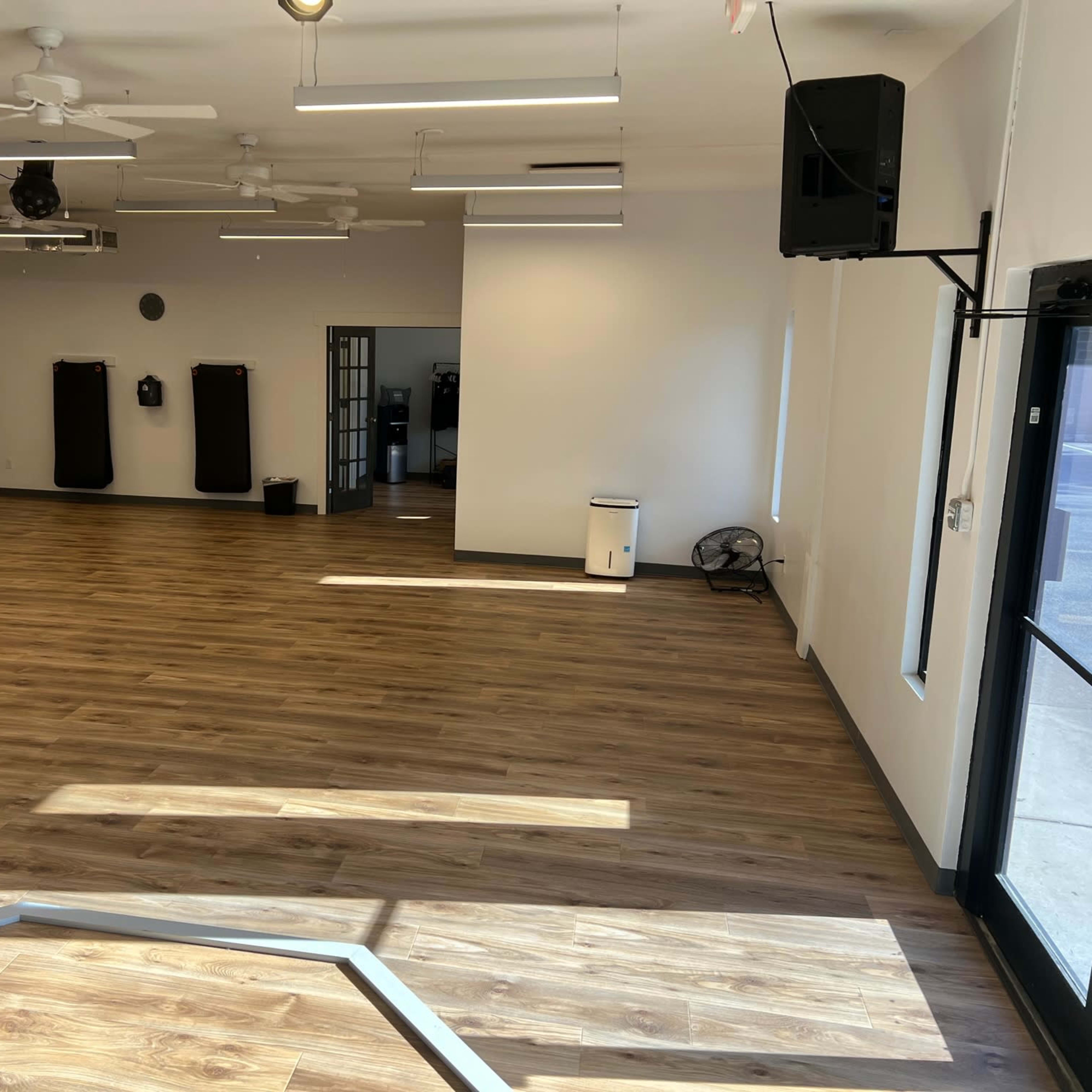 A spacious, empty room with wooden flooring, ceiling fans, and several fitness equipment stations along the walls.