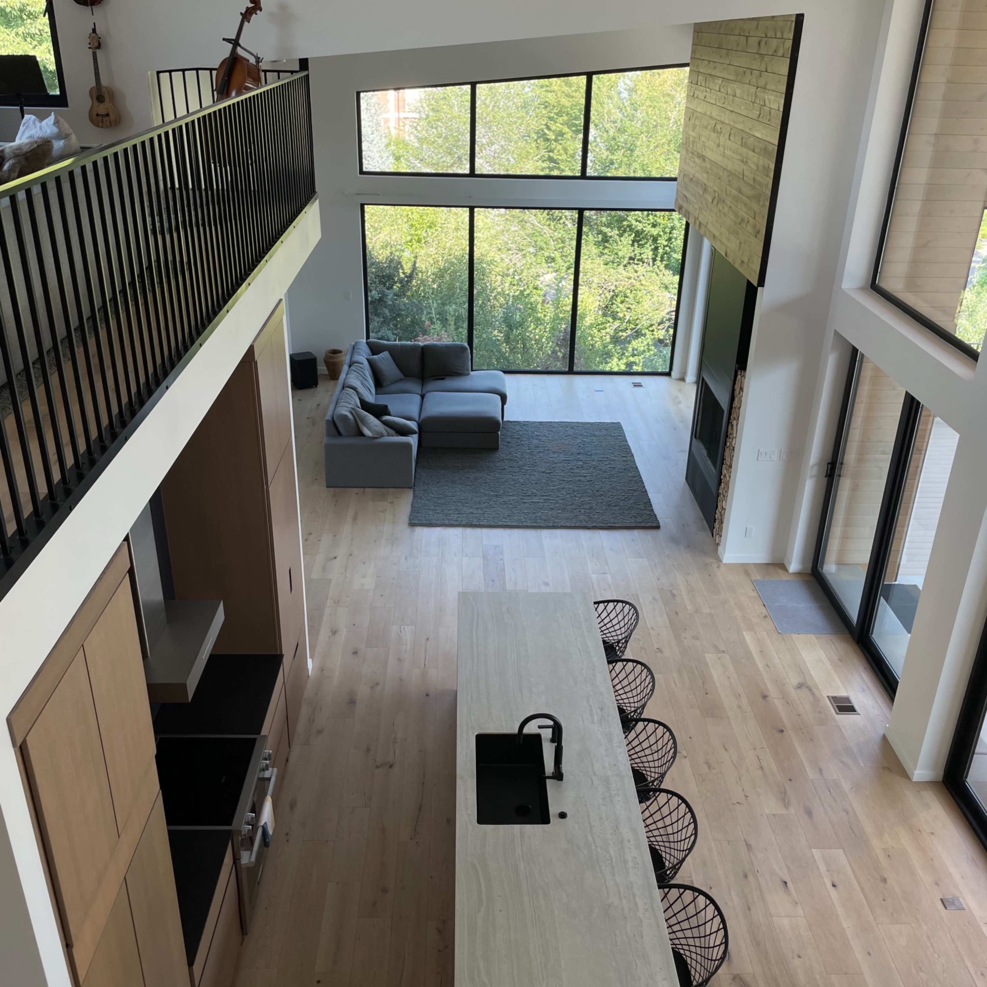 A modern open-concept living area with a kitchen island, seating area, and large windows overlooking greenery.