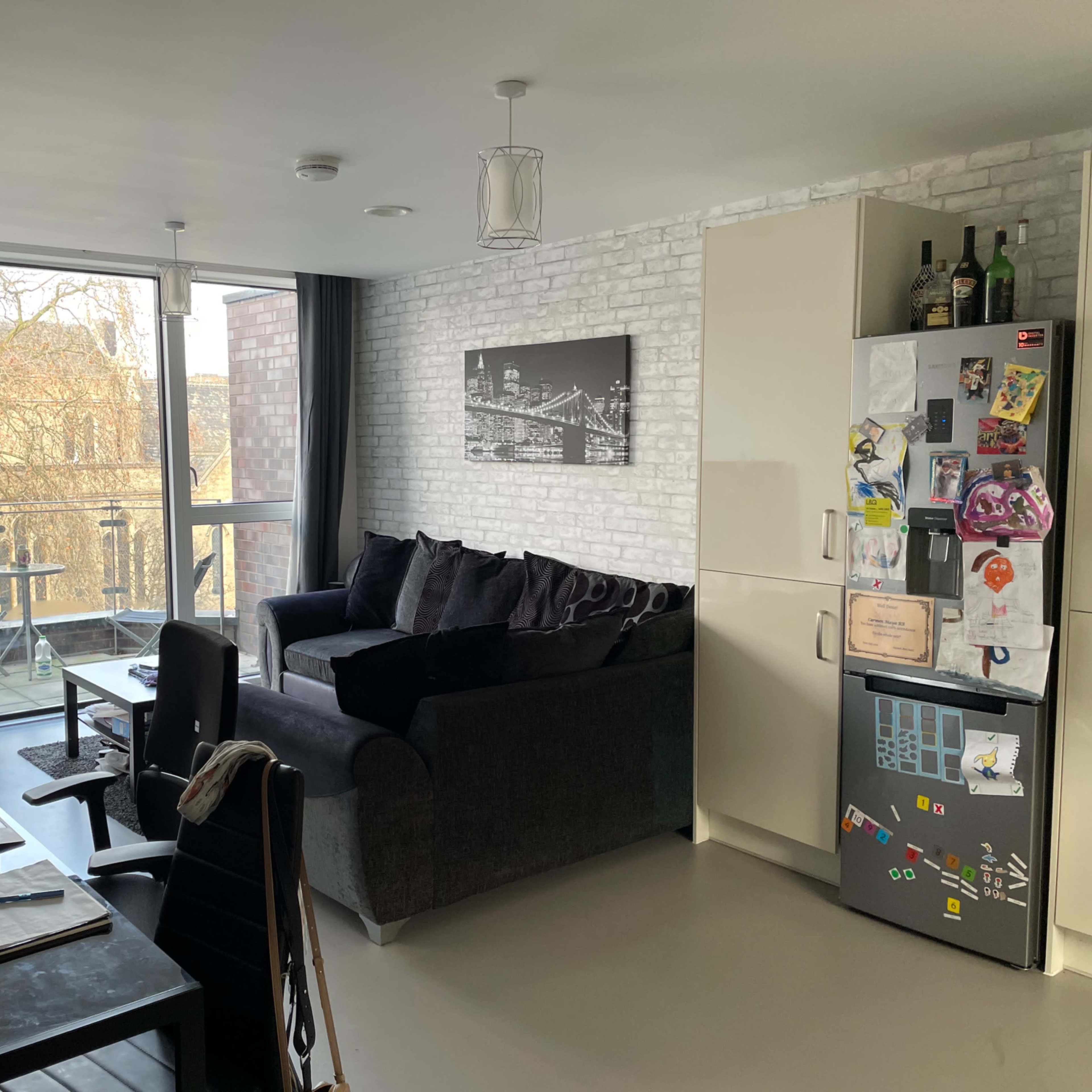 A modern living space featuring a sofa, a small dining area, and a kitchen with a refrigerator adorned with various magnets and items.