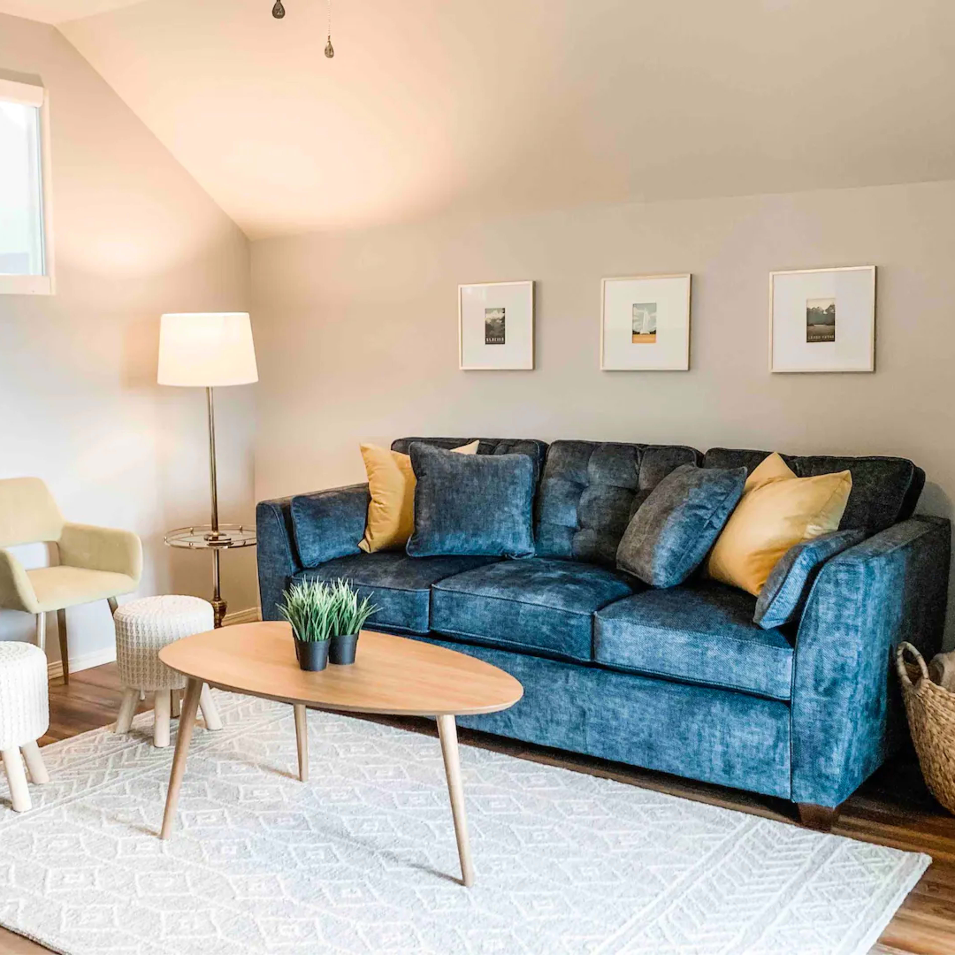 A cozy living room with a blue couch, two yellow chairs, a round coffee table, and a patterned rug.