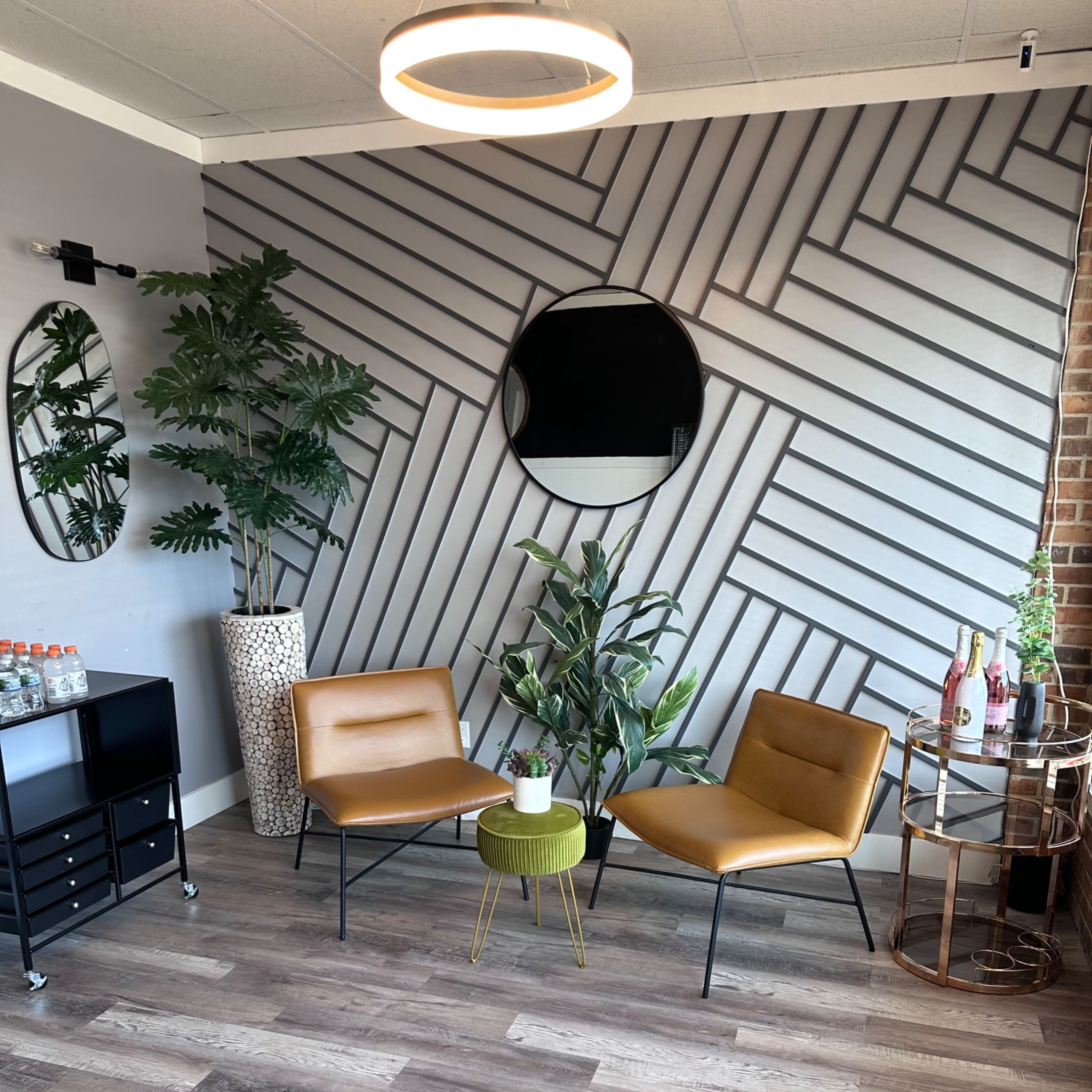 A modern lounge area with two leather chairs, a small round table, plants, and a decorative wall featuring geometric patterns.