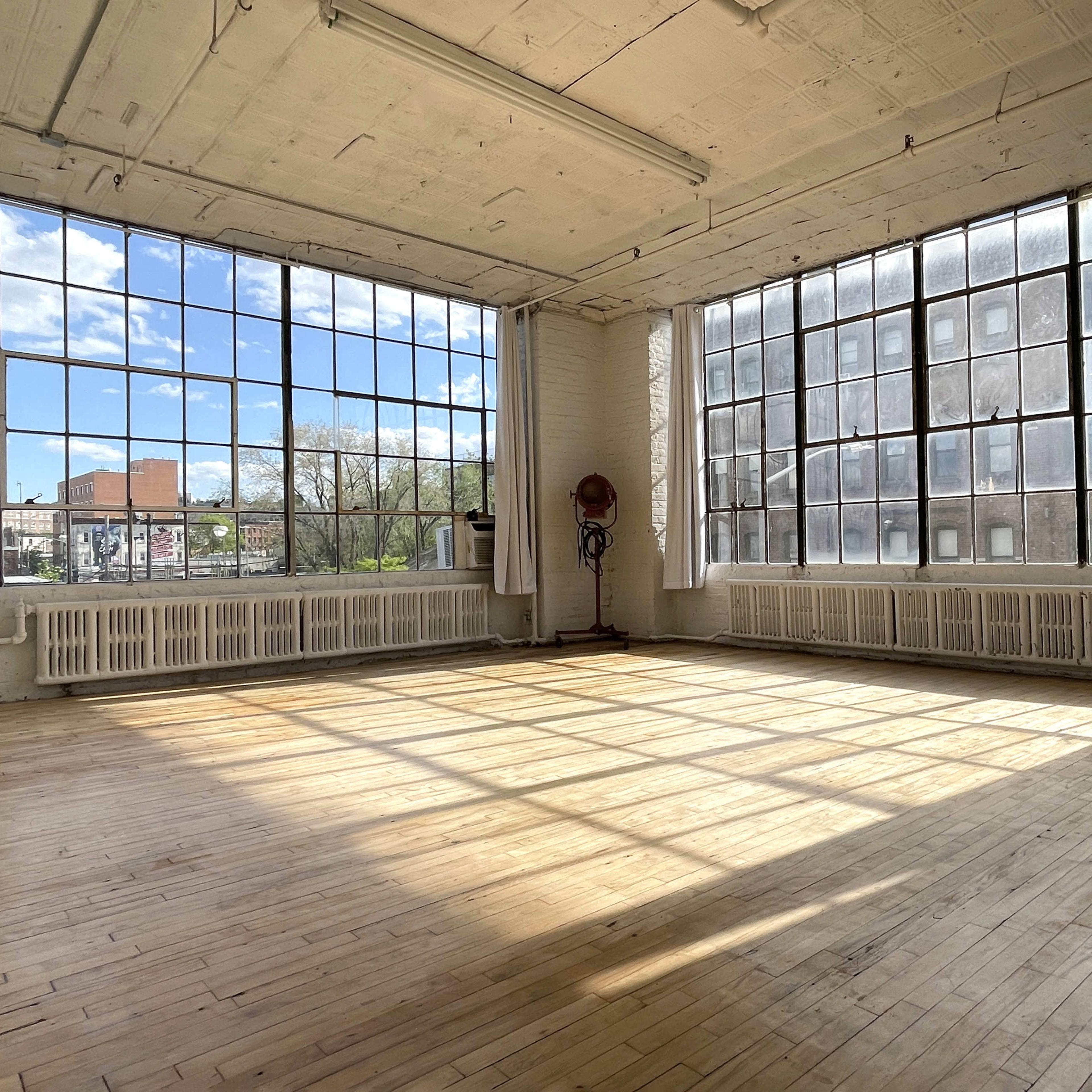 A spacious, empty room with large windows allowing natural light to fill the wooden floor.