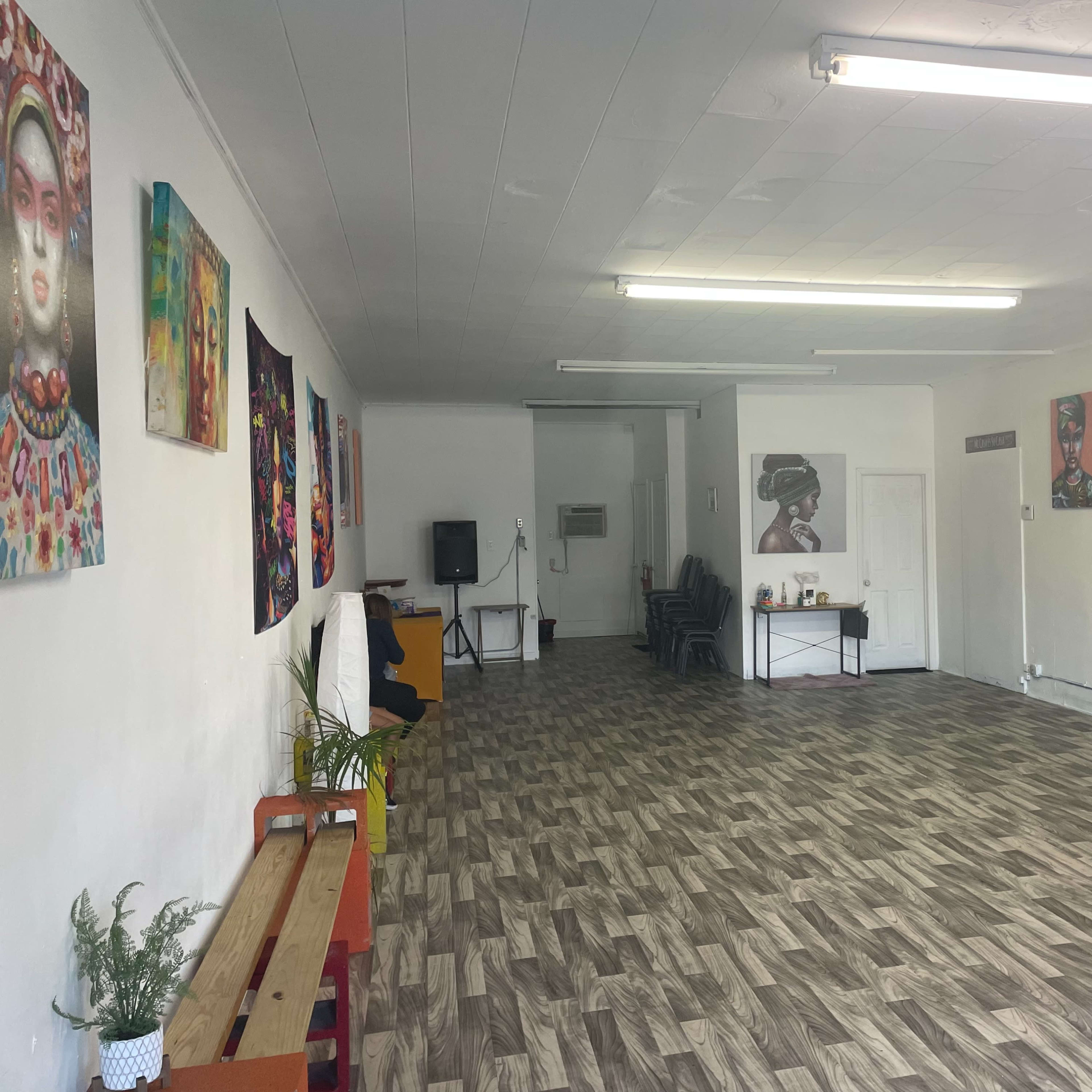 A spacious, well-lit room with a wooden floor, adorned with vibrant wall art, and featuring a large mirror on one side.