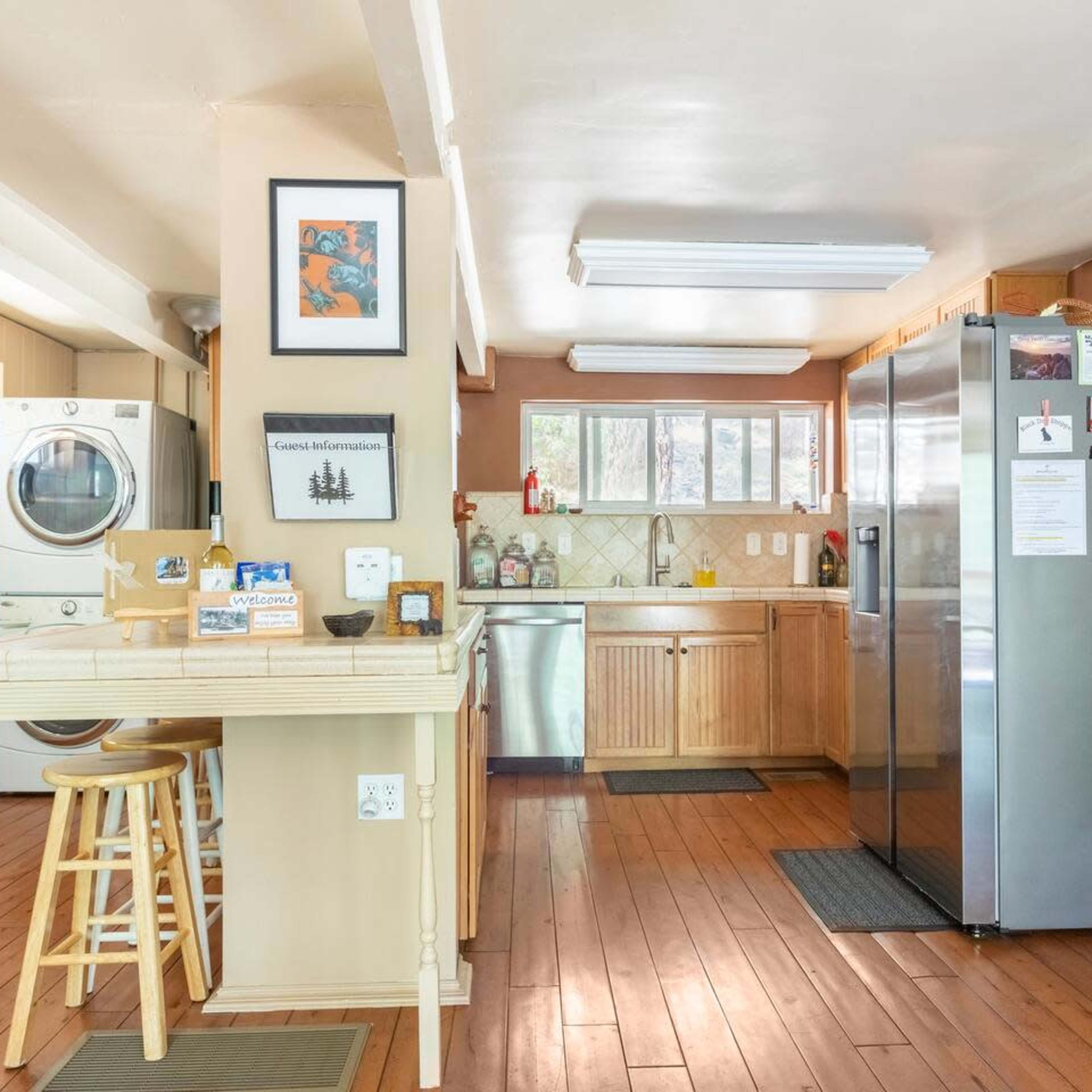A kitchen with wooden cabinetry, stainless steel appliances, a laundry area, and a small wooden table with stools.