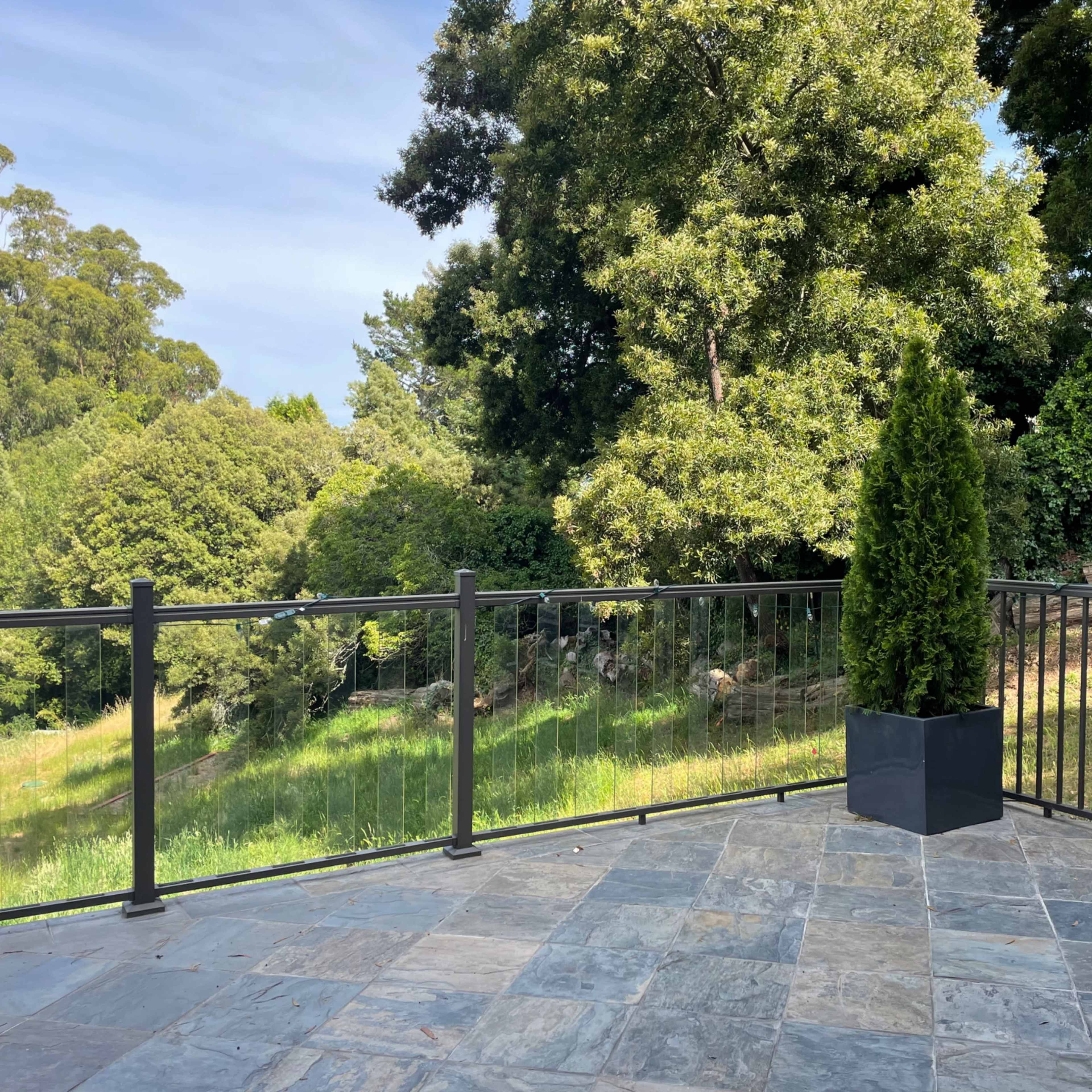 A stone patio with a black railing overlooks a greenery-filled landscape.