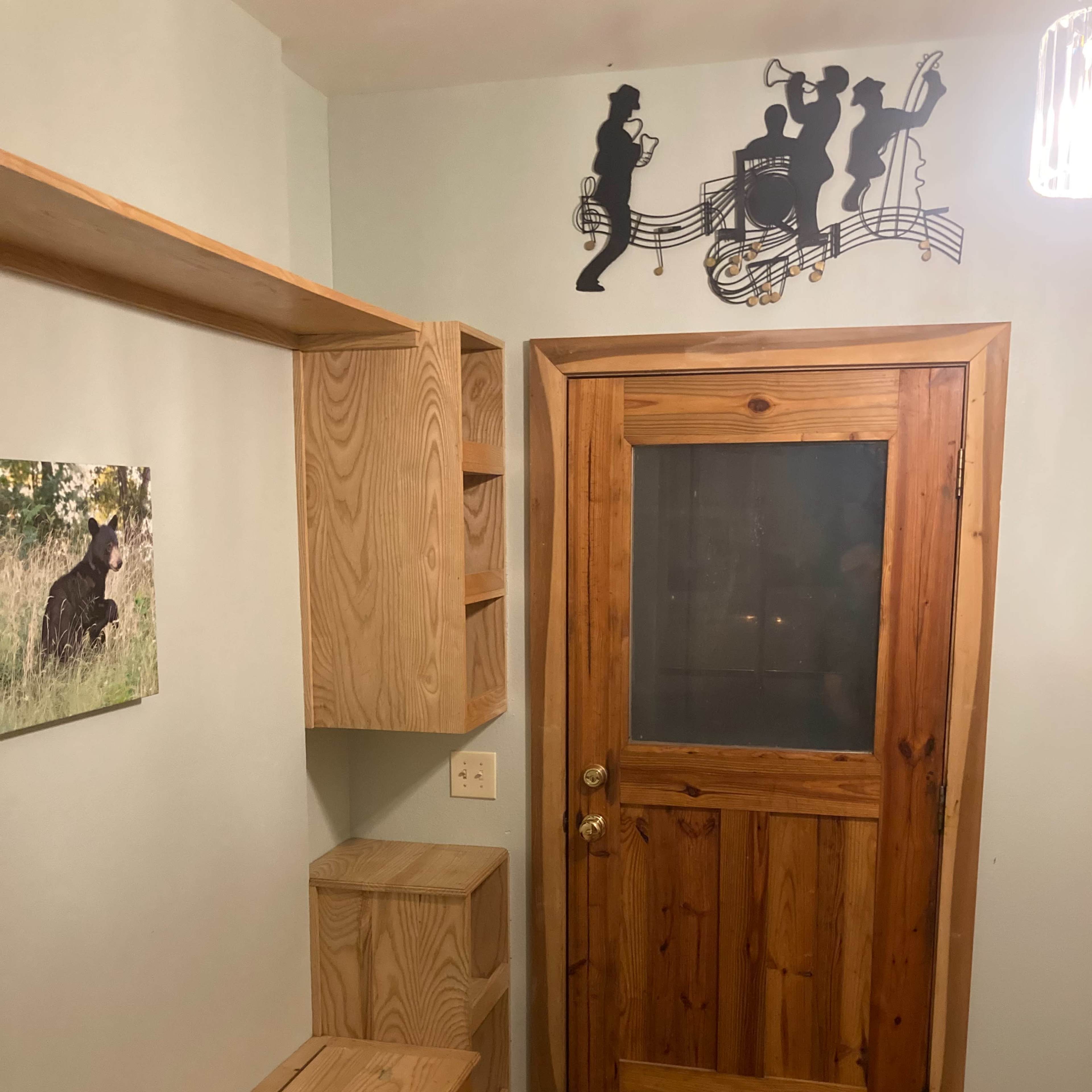 A wooden entryway with a door, built-in shelves, a bench, and a decorative musical silhouette mounted on the wall.